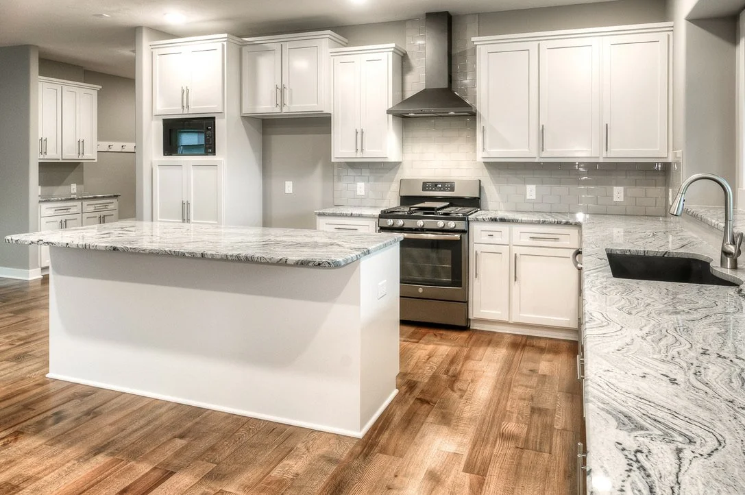 Modern kitchen with white cabinets, granite countertops, a central island, stainless steel stove, microwave, black sink, and hardwood floors.