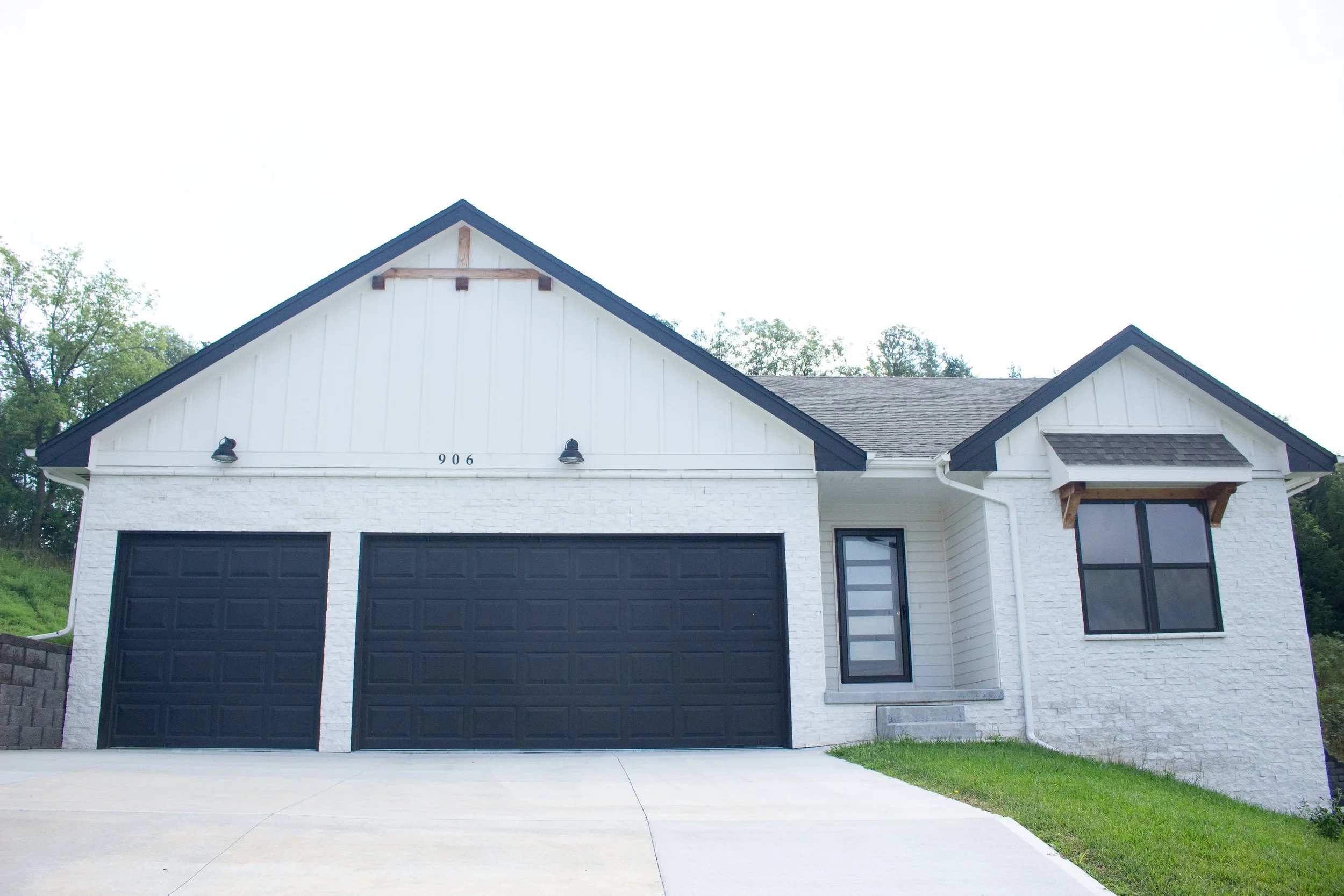 Front view of a modern two-story house with white brick and siding, black garage door, front door, and window, with a small lawn and concrete driveway.