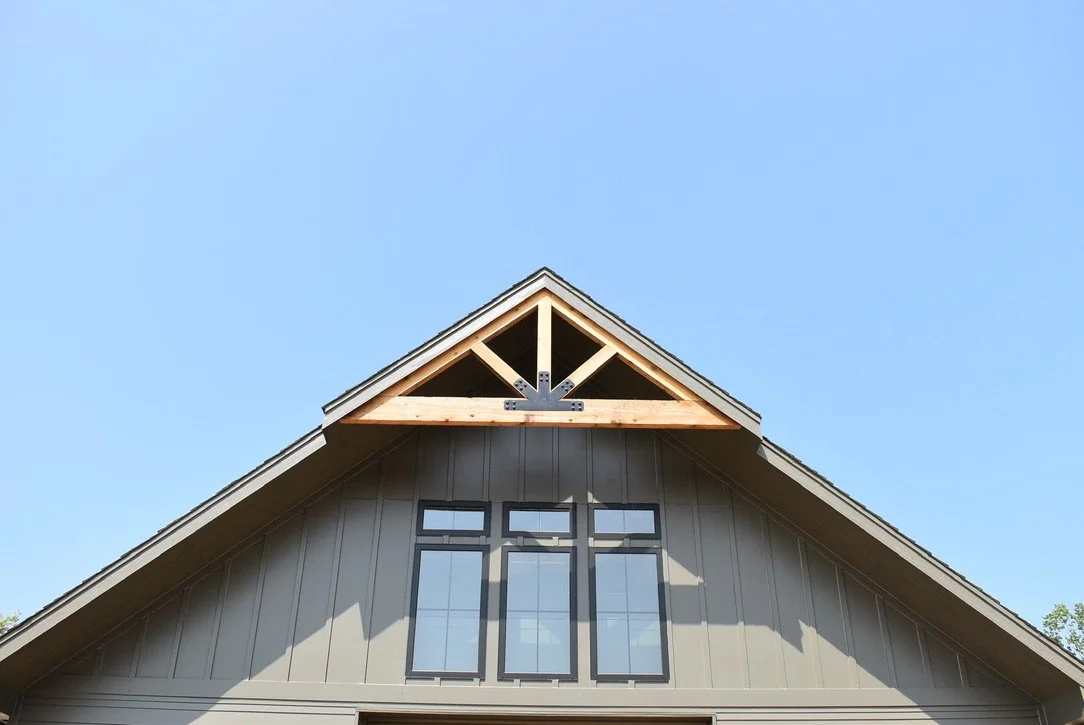 Front view of a house with a gabled roof, large window, and exposed roof trusses under the eaves, against a clear blue sky.
