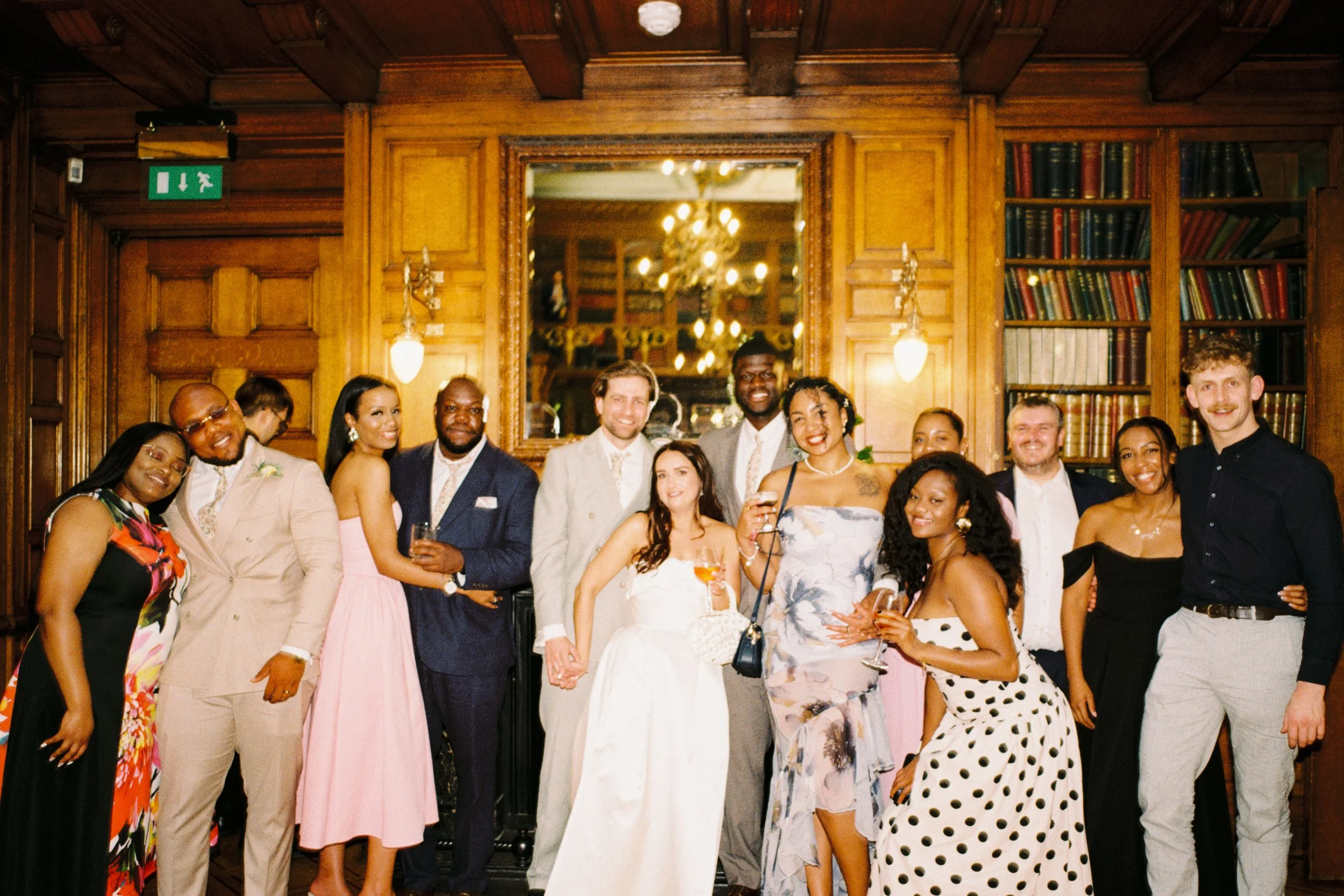 Group of diverse people celebrating at a social event in a wood-paneled room, some holding drinks, smiling, dressed in formal and semi-formal attire.