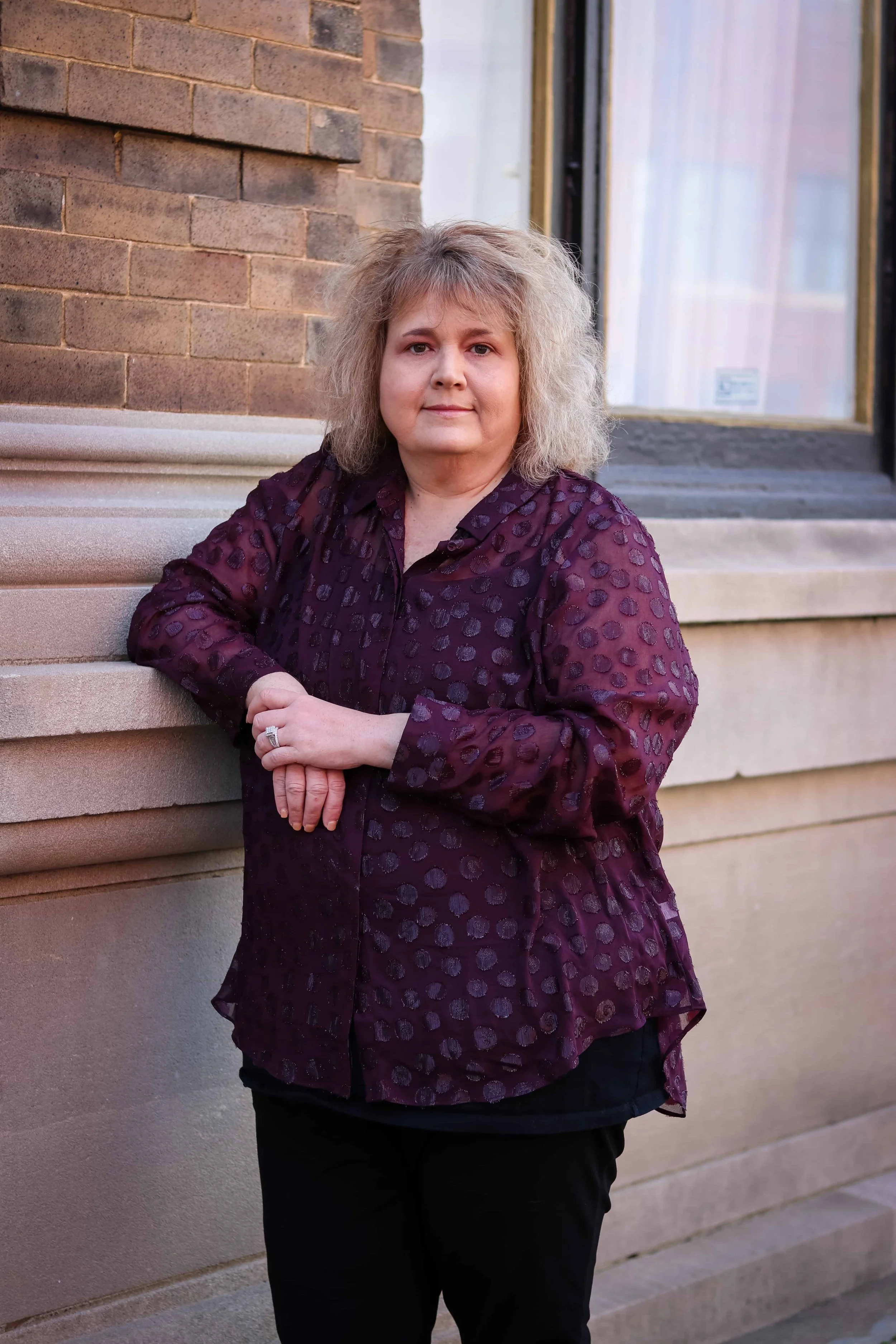 Woman leaning against a building with one arm while posing for an outdoor portrait.