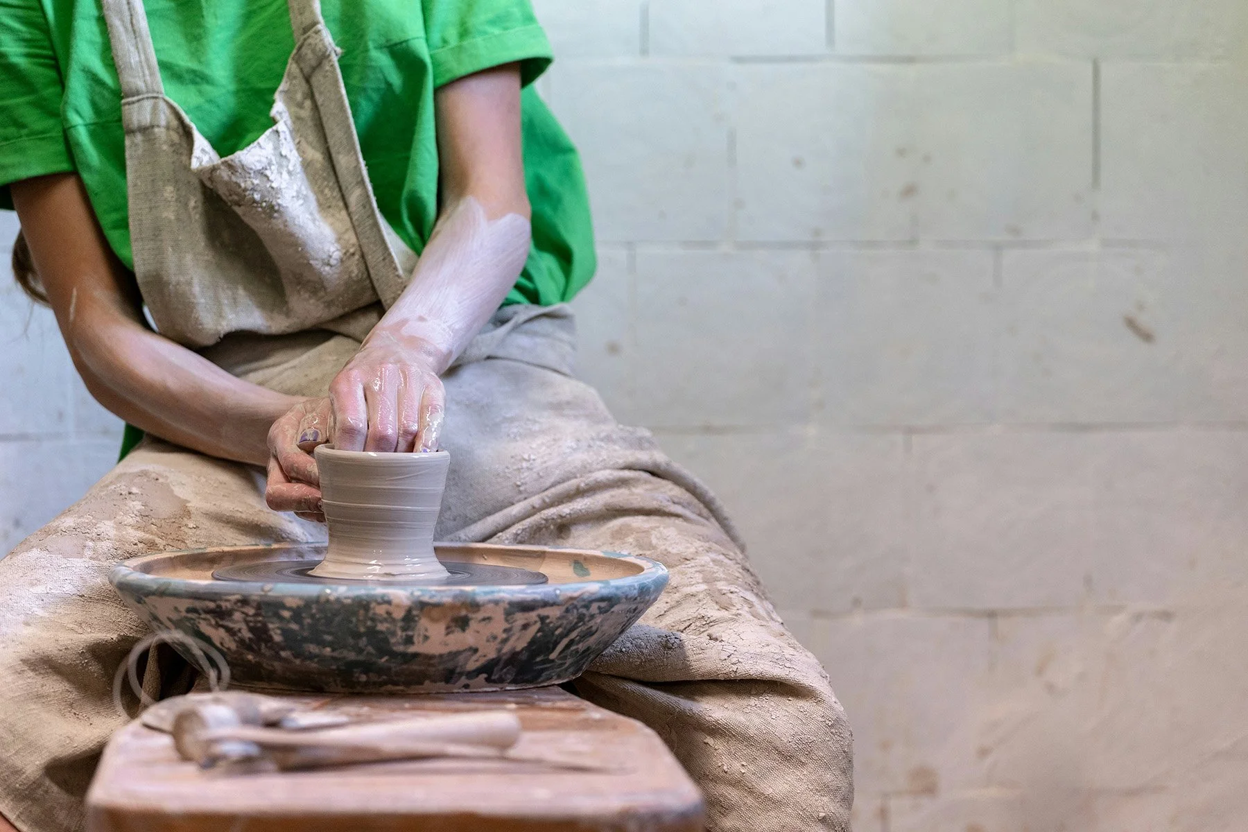 Ceramic artist shaping a clay pot on a pottery wheel in a pottery studio.