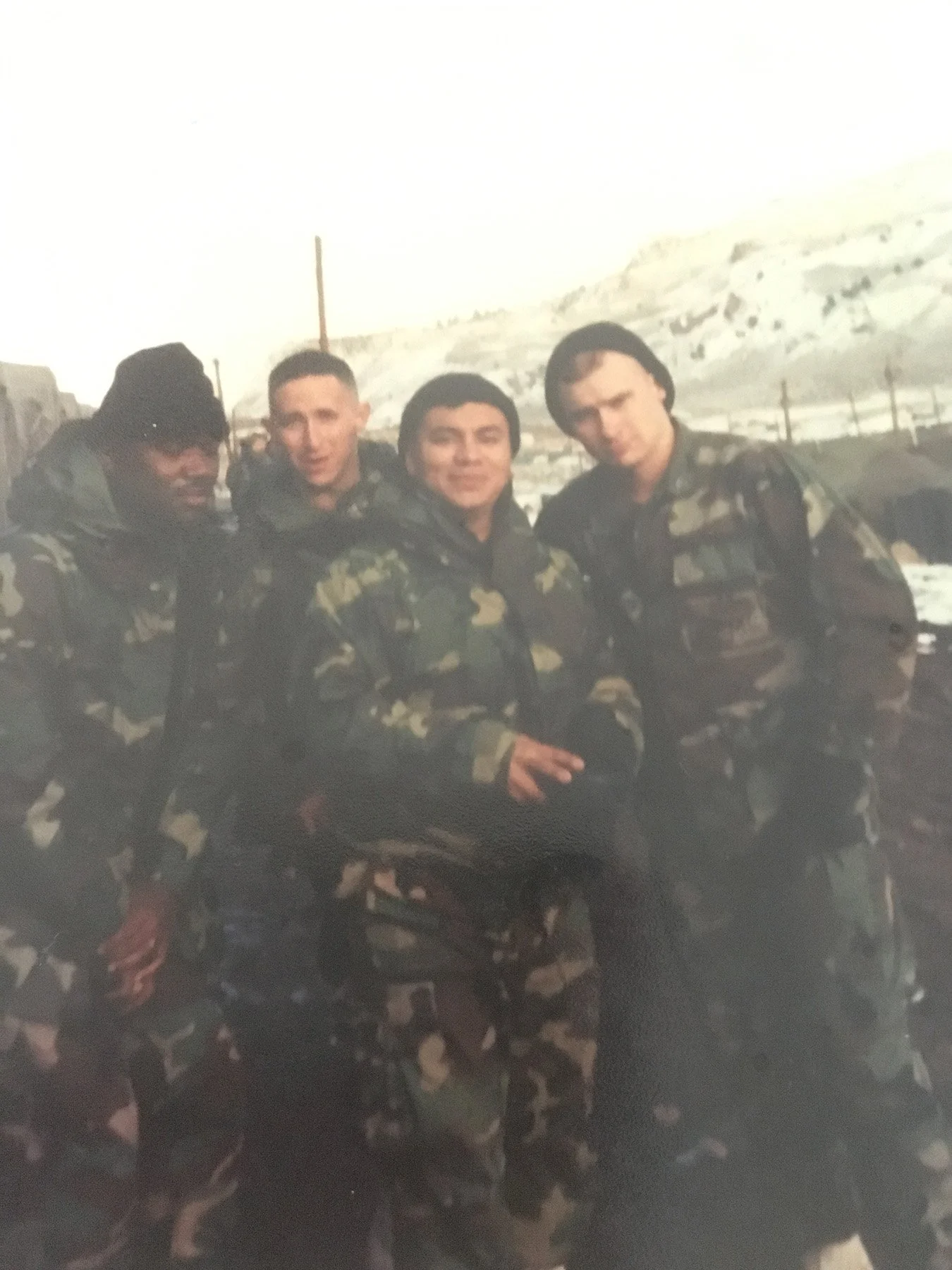 Four young Marines in camouflage uniforms standing together outdoors in a snowy military setting during deployment training or service.