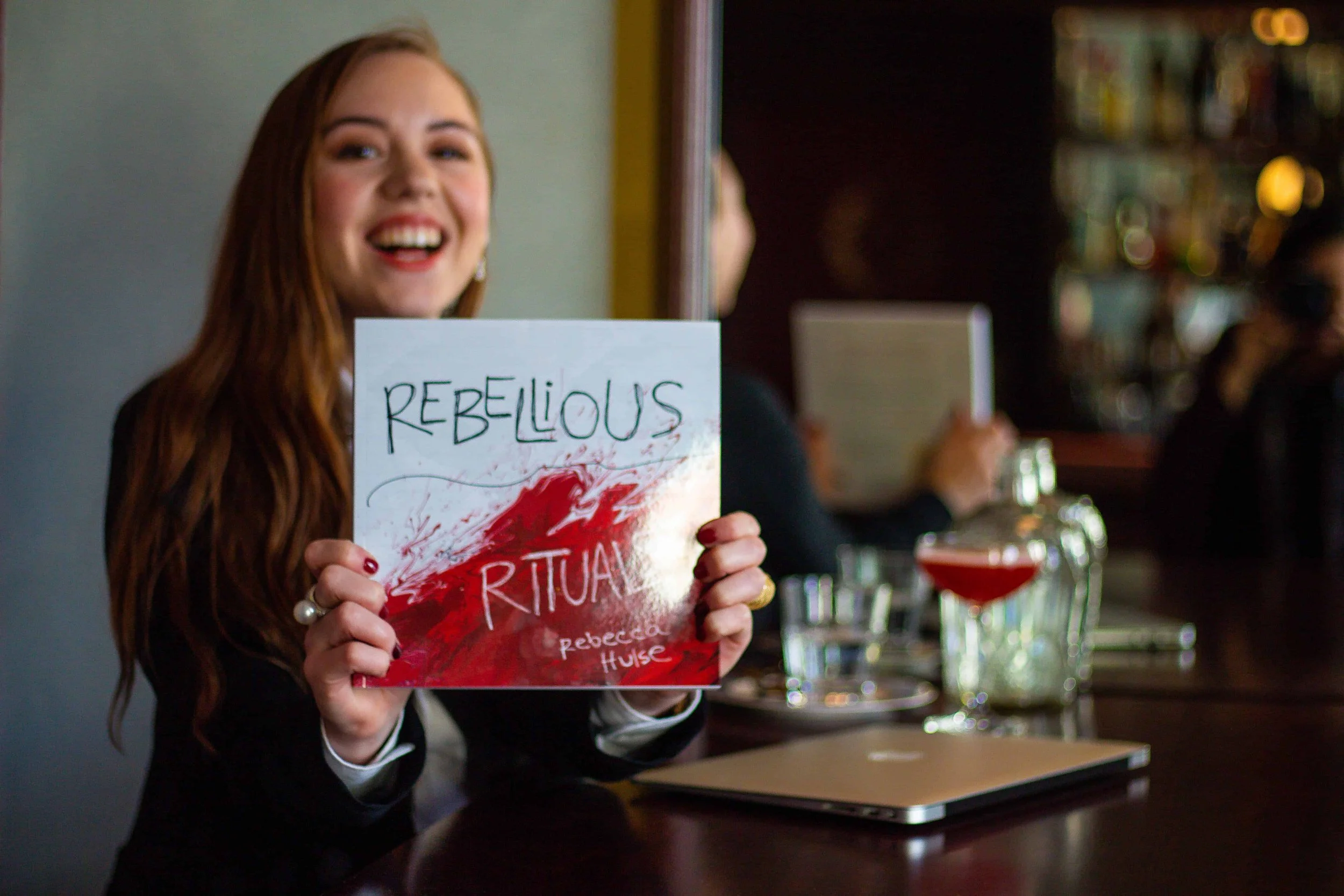 Author smiling while holding a copy of her book, Rebellious Rituals.
