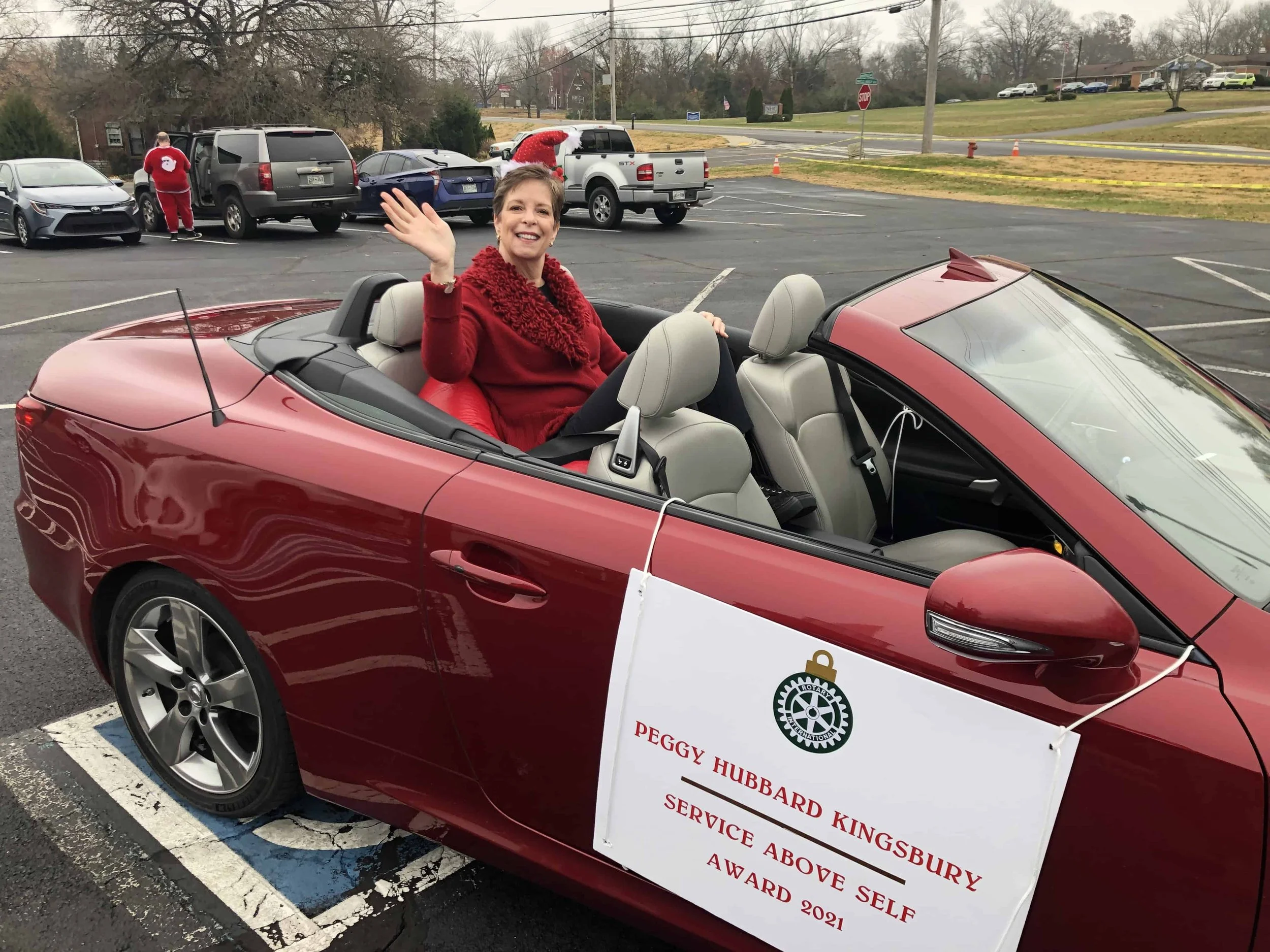 Woman waving from a red convertible during a community parade after receiving a Service Above Self award.