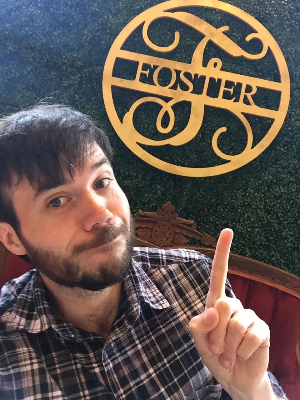 Man points toward a decorative wall sign with the name Foster while seated in a restaurant booth.