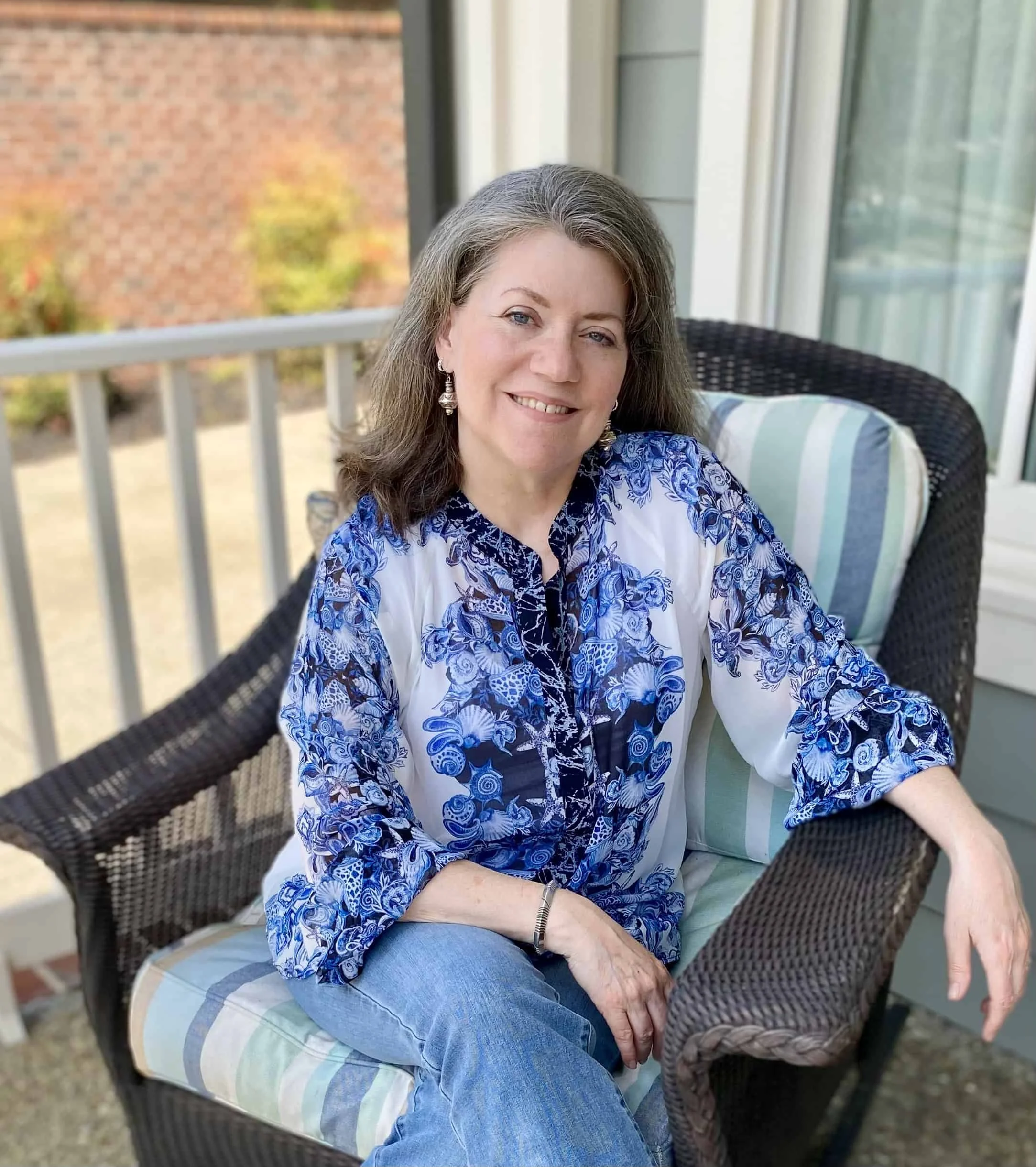 Silver-haired woman in a blue printed blouse sitting in a chair on a patio.