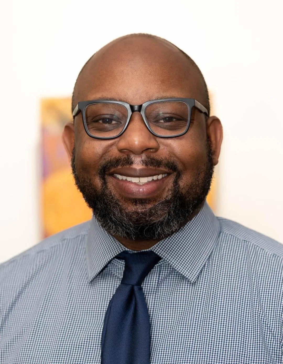Black man with a beard and black frame glasses smiles at the camera for a headshot portrait.