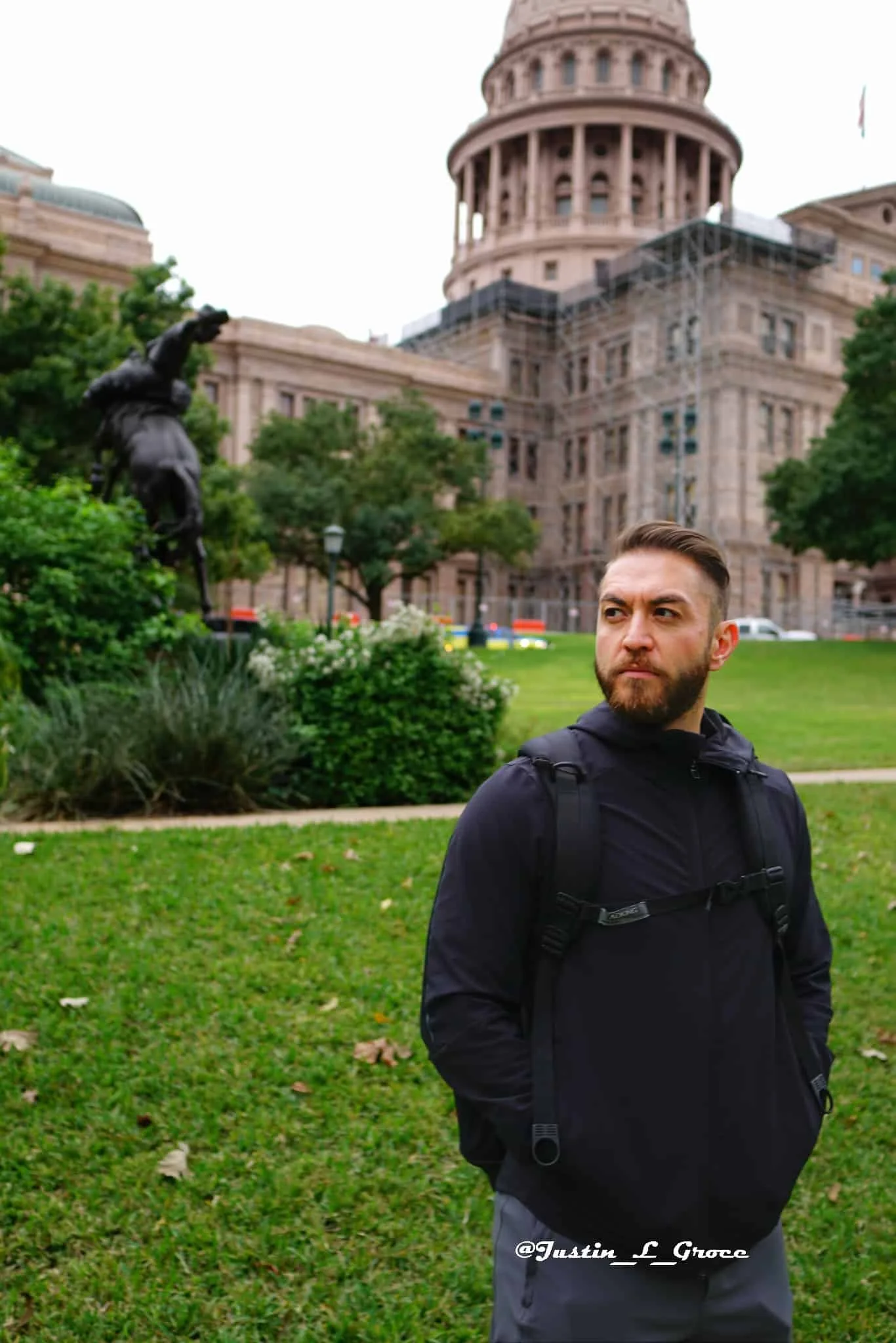 Man looking off into the distance with a statue and historic building behind him.