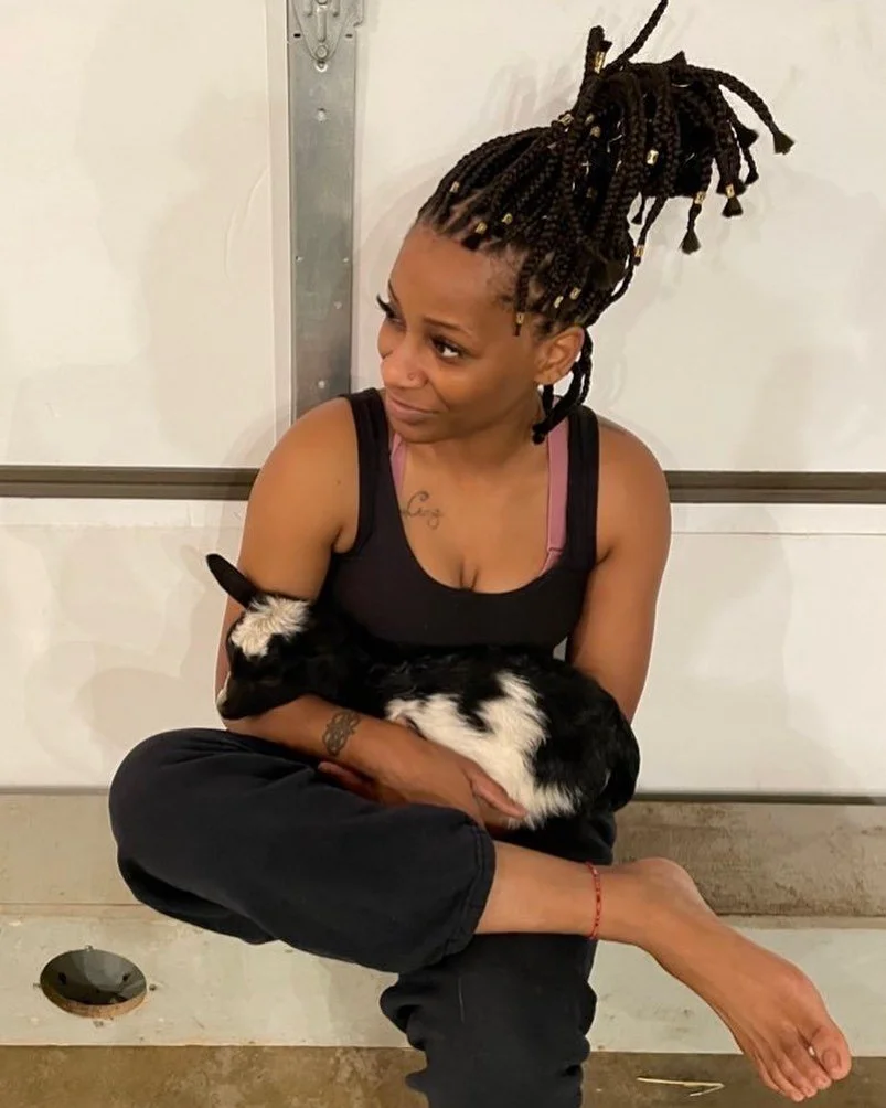 Seated woman holds baby goat in her arms.