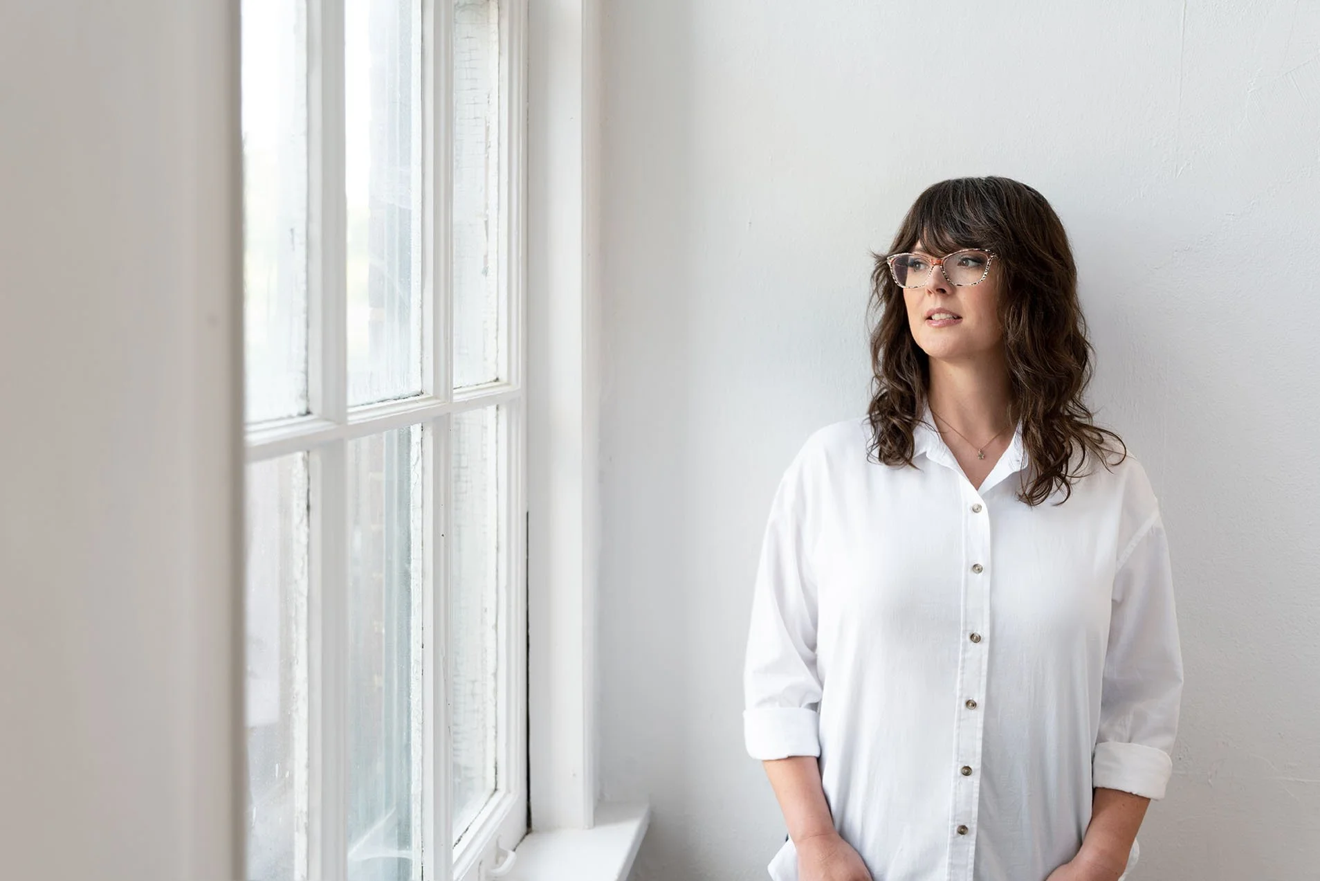 Brandi Fleck standing by a window in natural light for the Human Amplified bonus episode “Coming Home.”