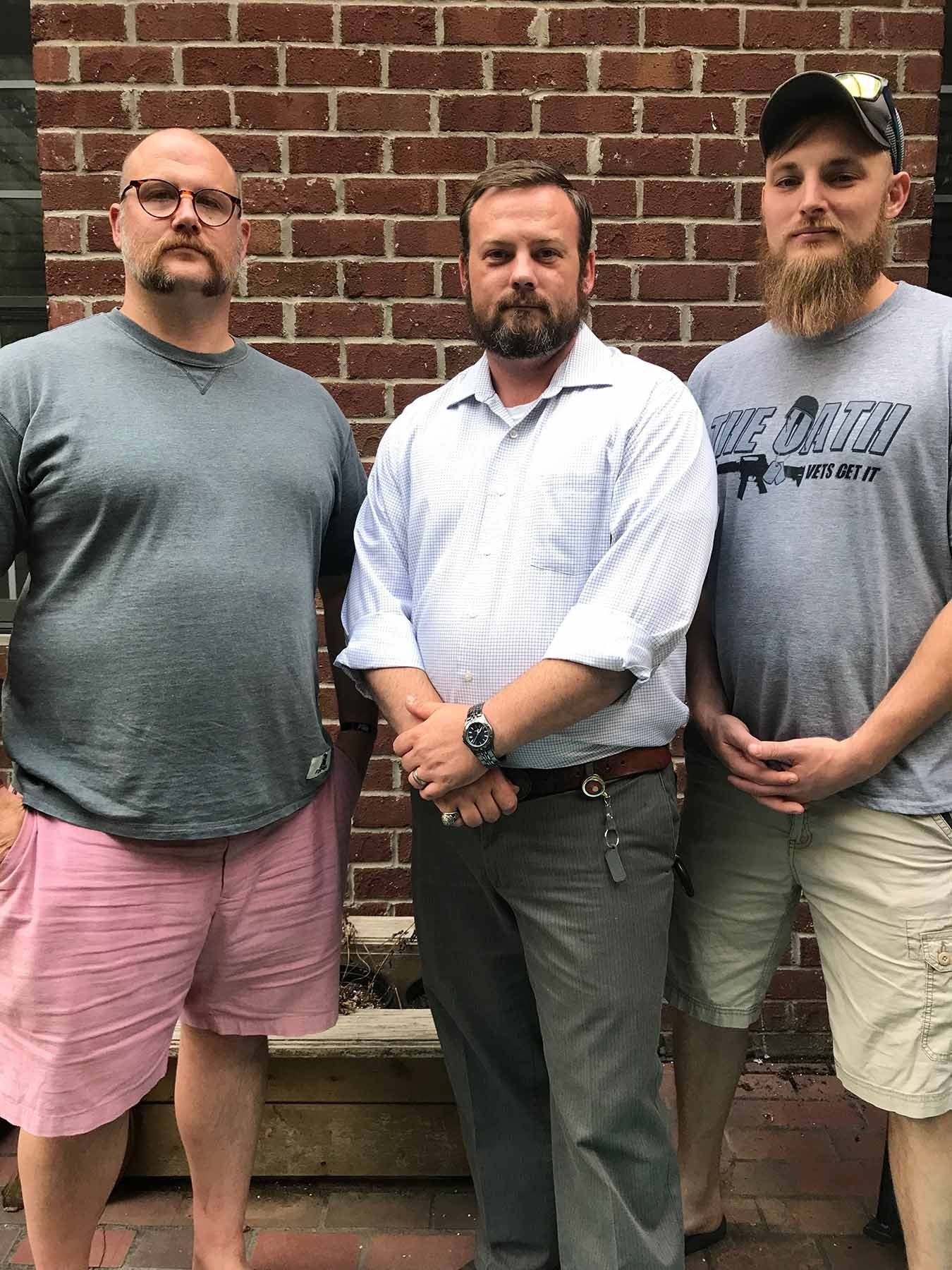 Three Marine veterans posing together outside in casual clothing in front of a brick building.