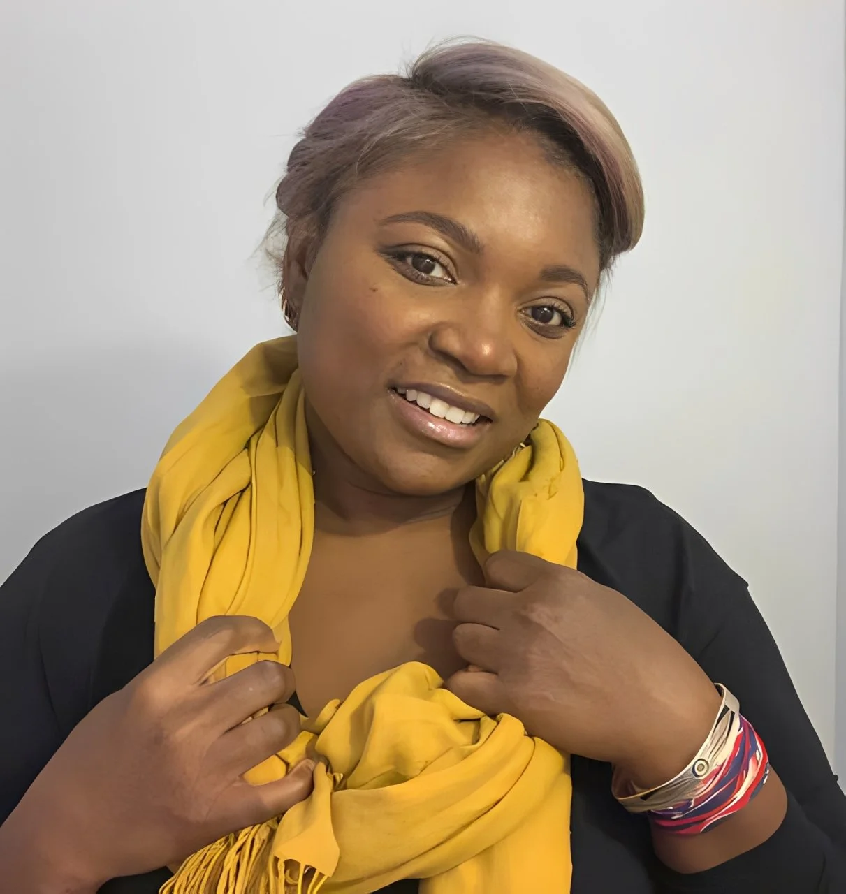 Woman smiles for portrait while holding a yellow scarf around her neck.