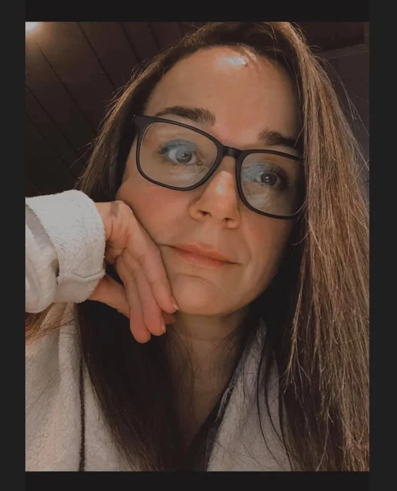 Close-up portrait of a woman wearing glasses and resting her chin on her hand.