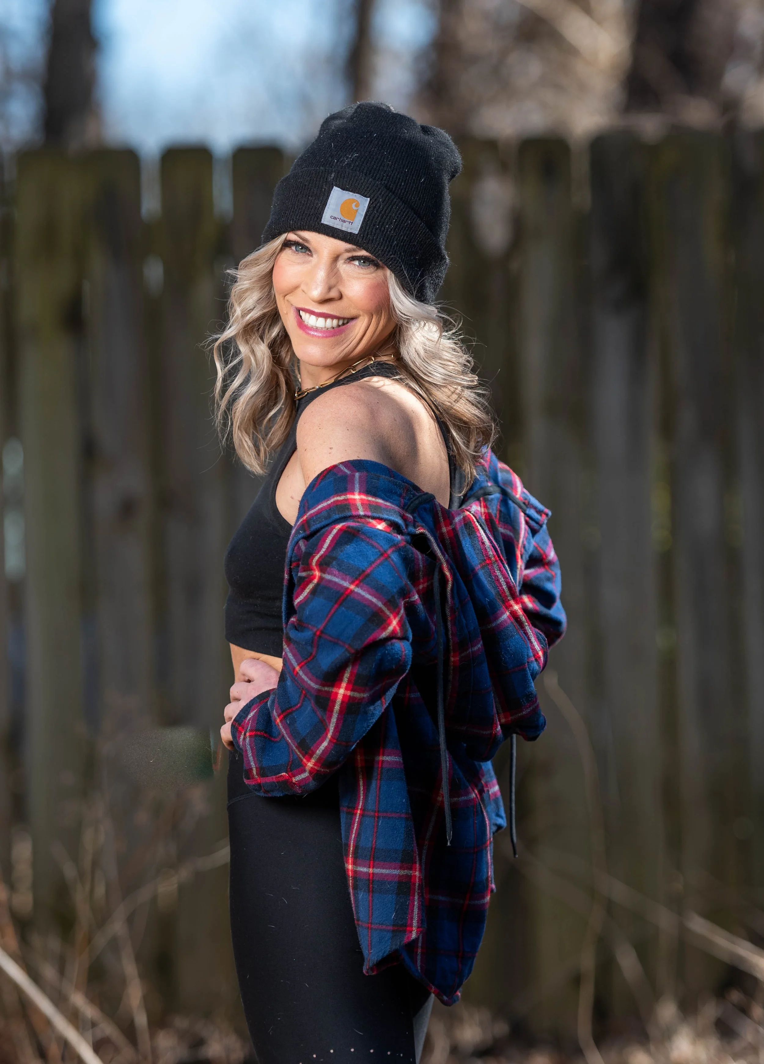 Smiling woman poses outdoors with hands on hips while looking back toward the camera.