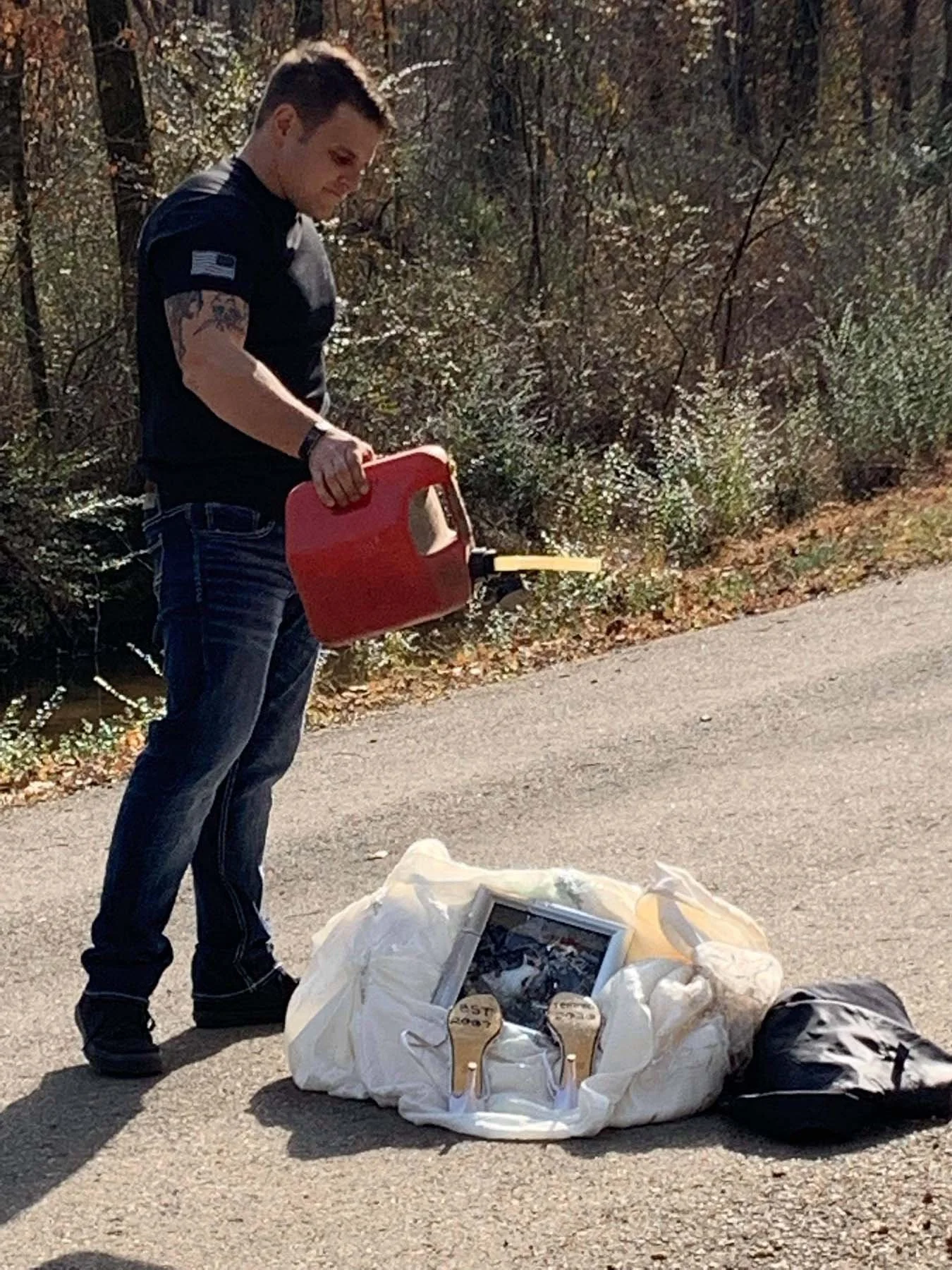 Man pouring gasoline on wedding keepsakes during a symbolic divorce ritual outdoors.
