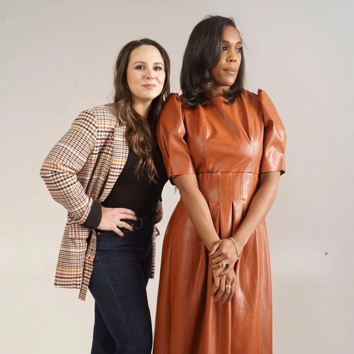 Two female founders posing together in a studio, with one wearing a brown leather dress and the other a plaid blazer.