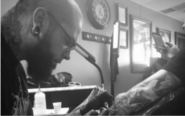 Black and white photo of a tattoo artist working on a detailed arm tattoo inside a professional tattoo studio in Franklin, Tennessee.