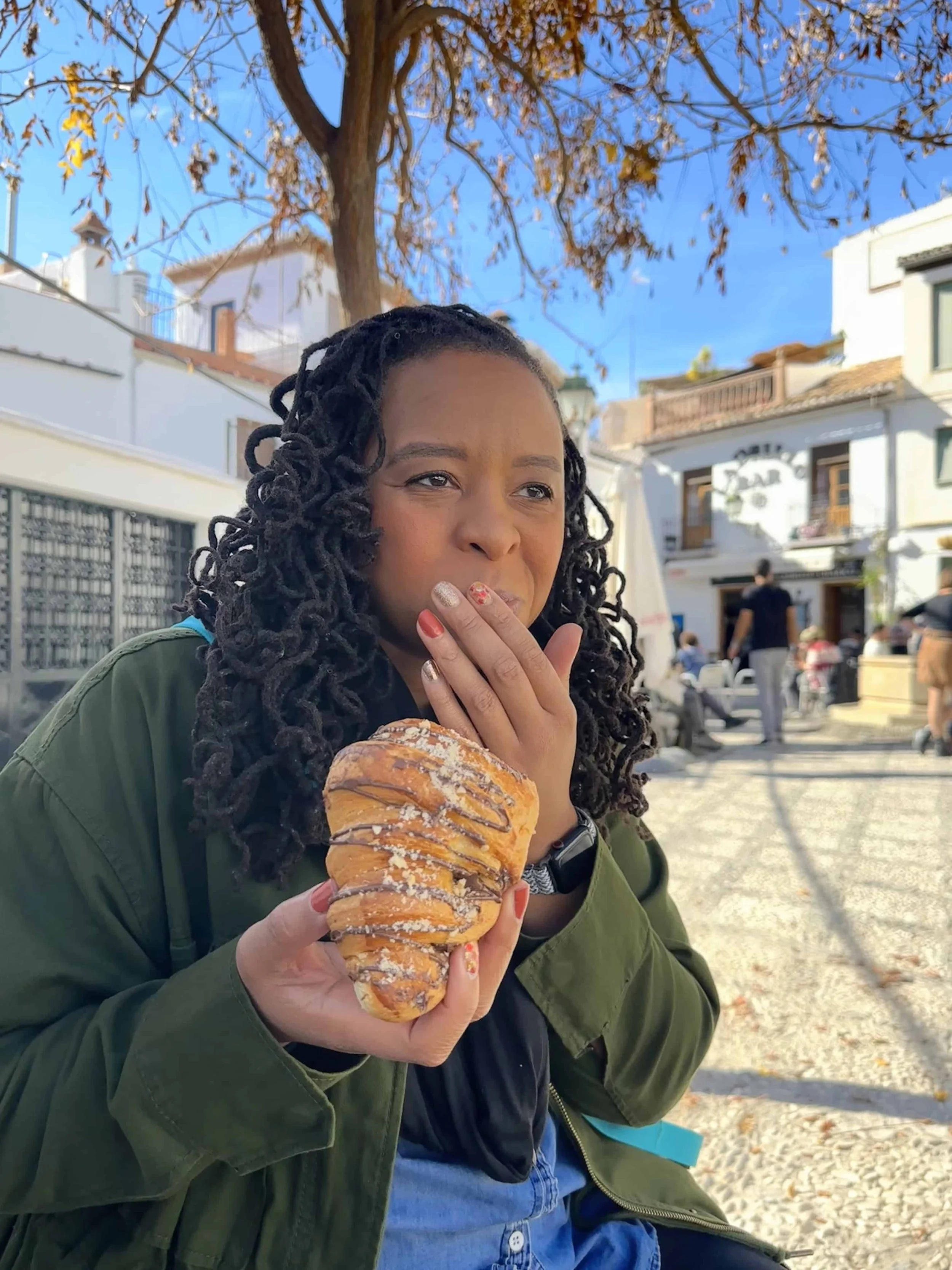 Woman sitting outside eating croissants.