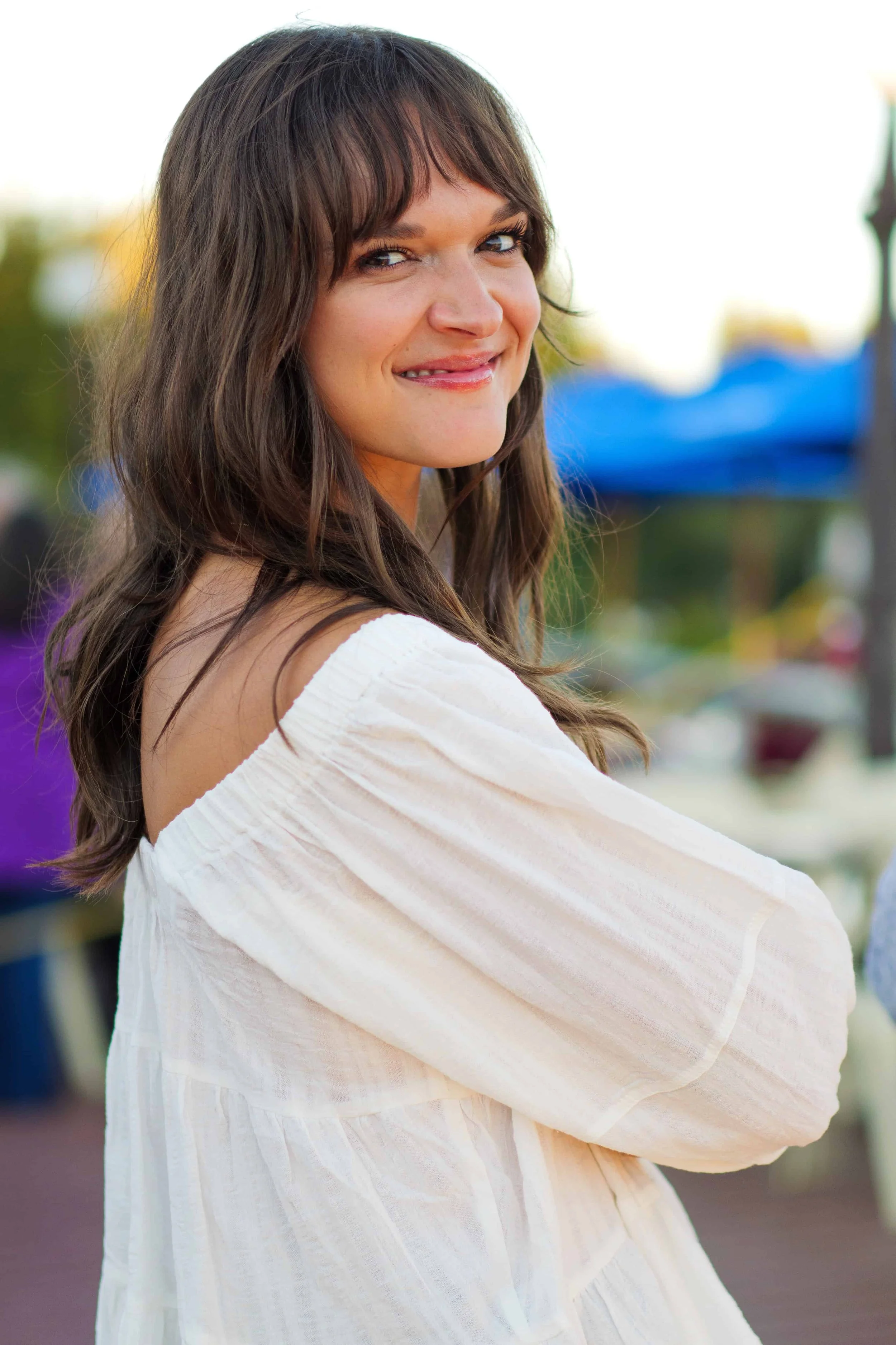Smiling brunette woman with bangs looking over her shoulder for a portrait.