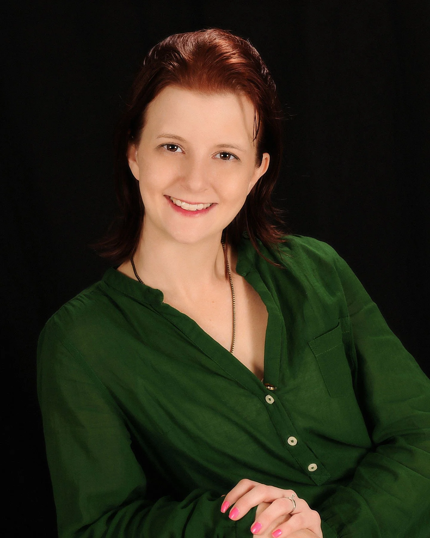Smiling preschool teacher wearing a green blouse against a black background.