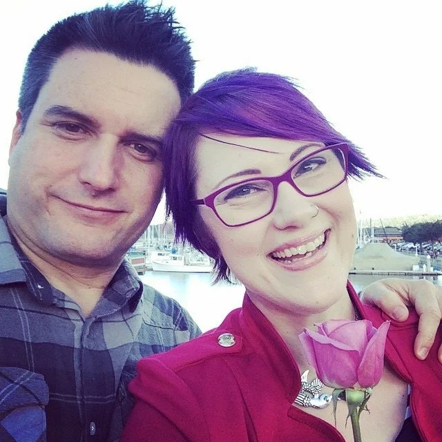 Couple smiling during a waterfront date, with a pink rose and marina in the background.