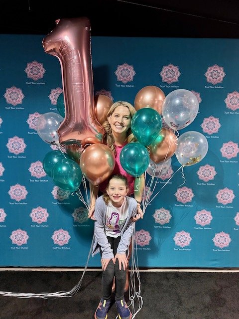 Woman celebrating one year of her intuitive work business with a young girl, surrounded by balloons.