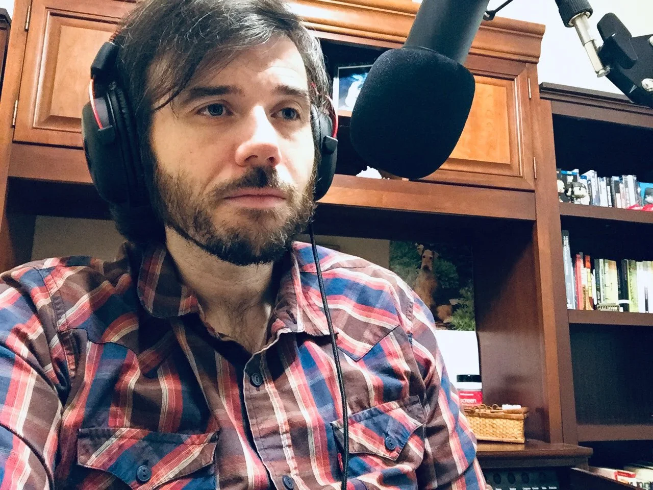 Man wearing headphones speaks into a microphone while recording a podcast in a home office.