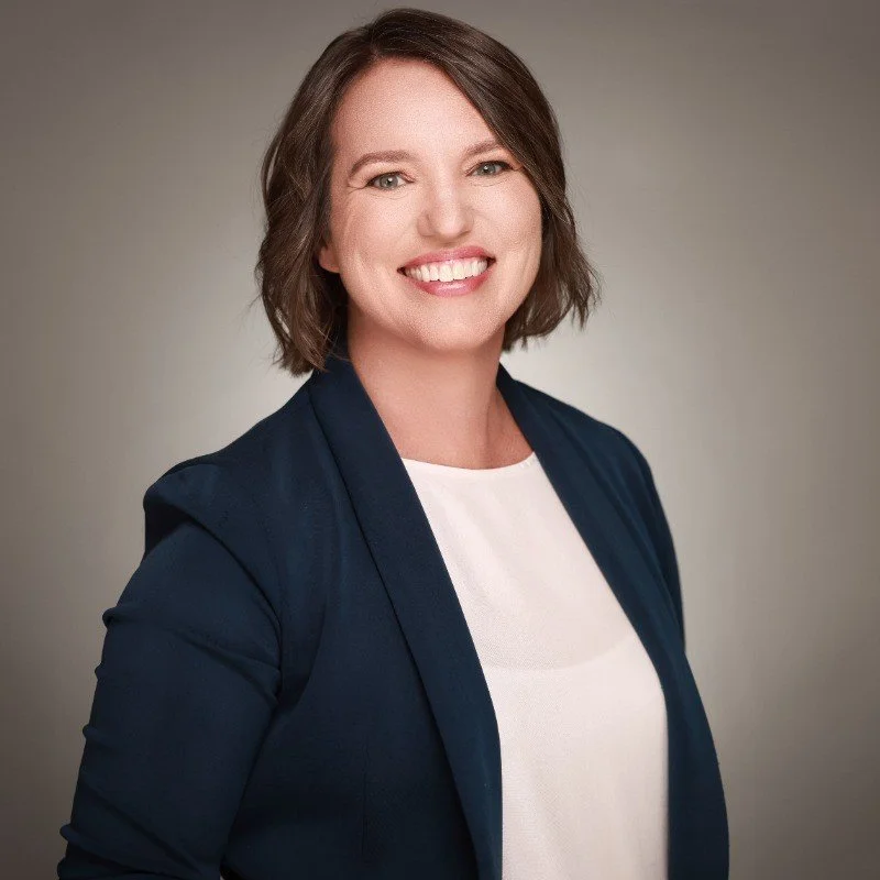 Brunette woman smiling for a portrait while wearing a navy blazer.
