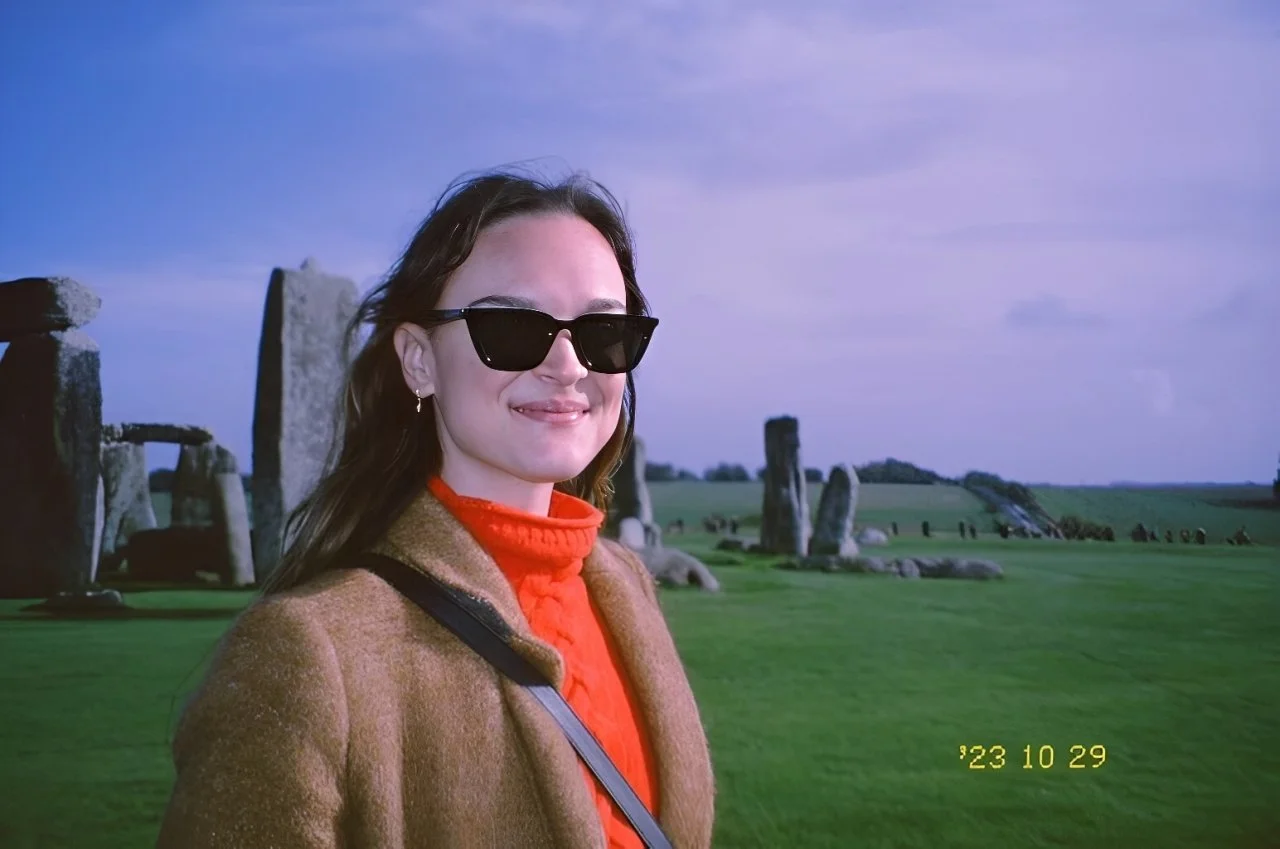 Brunette woman in sunglasses captured on film, standing near the Stonehenge monument.