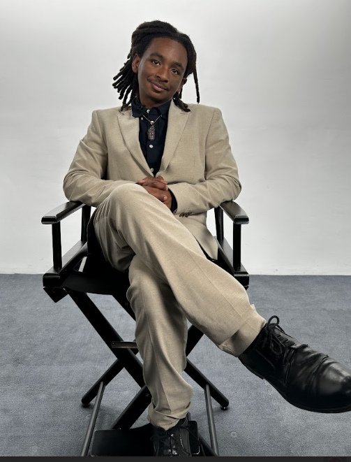 Lawrence C. Harris seated in a chair wearing a light suit, smiling confidently in a studio setting