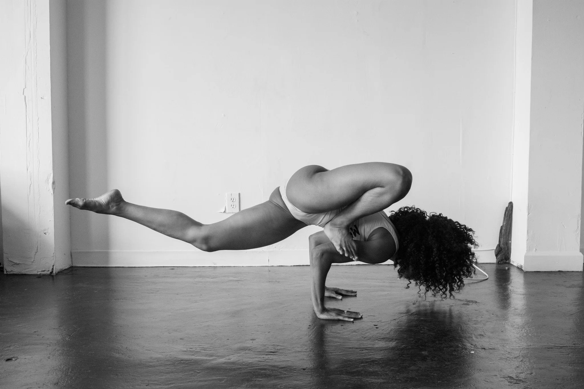 Black and white photo of woman doing an advanced balancing yoga pose.