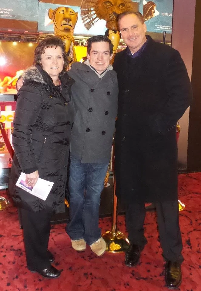 Parents and adult son smiling together at a public event.