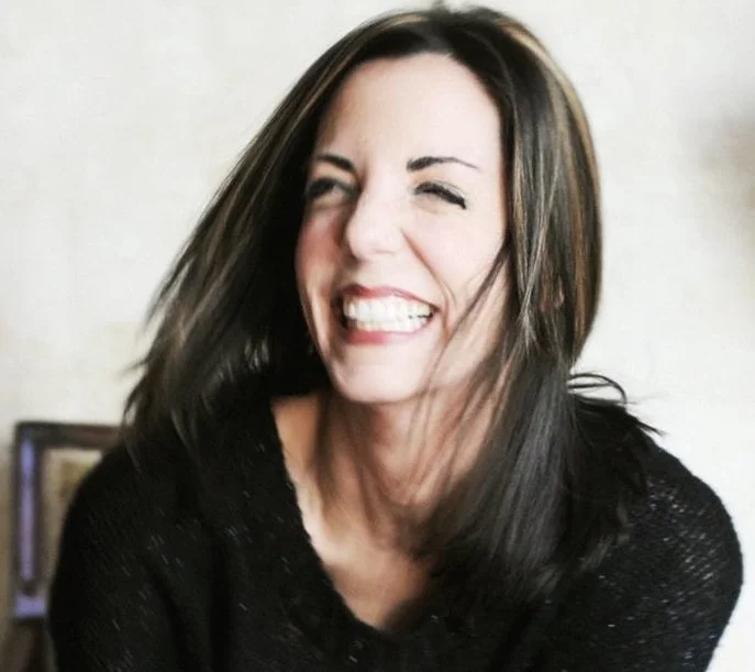 Smiling woman with dark hair laughing during a candid indoor portrait.