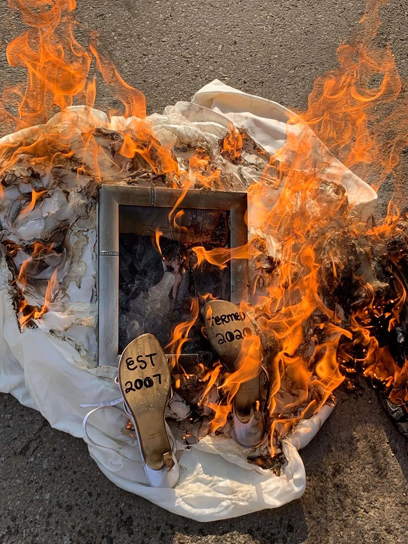 Wedding dress, shoes, and a framed photo burn during a symbolic post-divorce ceremony.