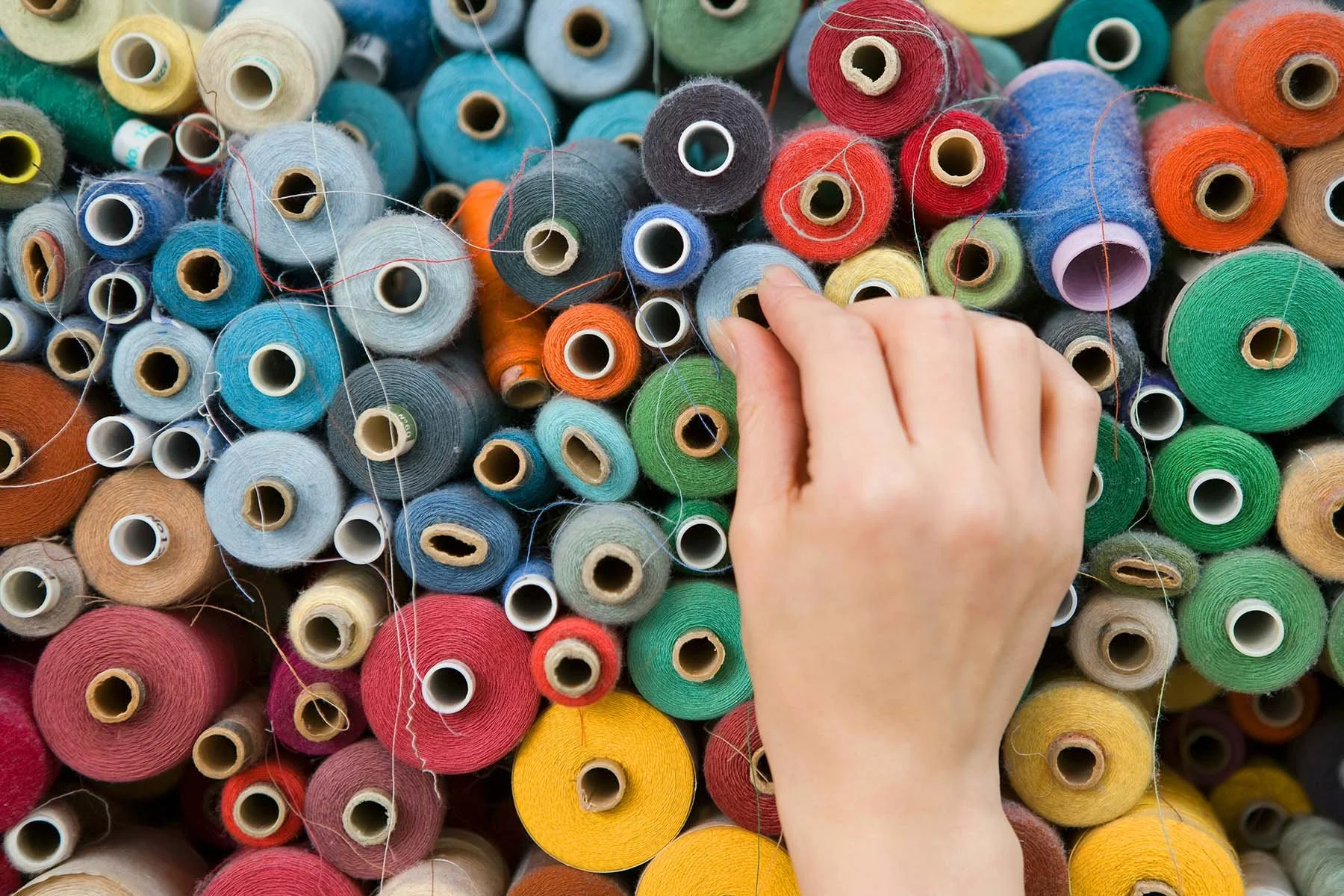 Hand selecting a colorful spool of thread from a collection of thread spools.