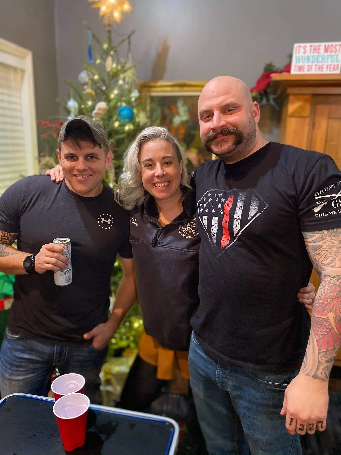 Three adults pose together at a Christmas gathering, reflecting a blended family dynamic.