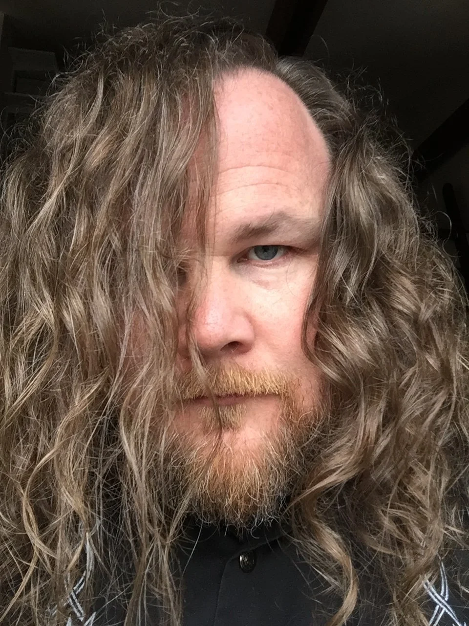 Close-up portrait of a person with long curly hair and a beard looking directly into the camera.