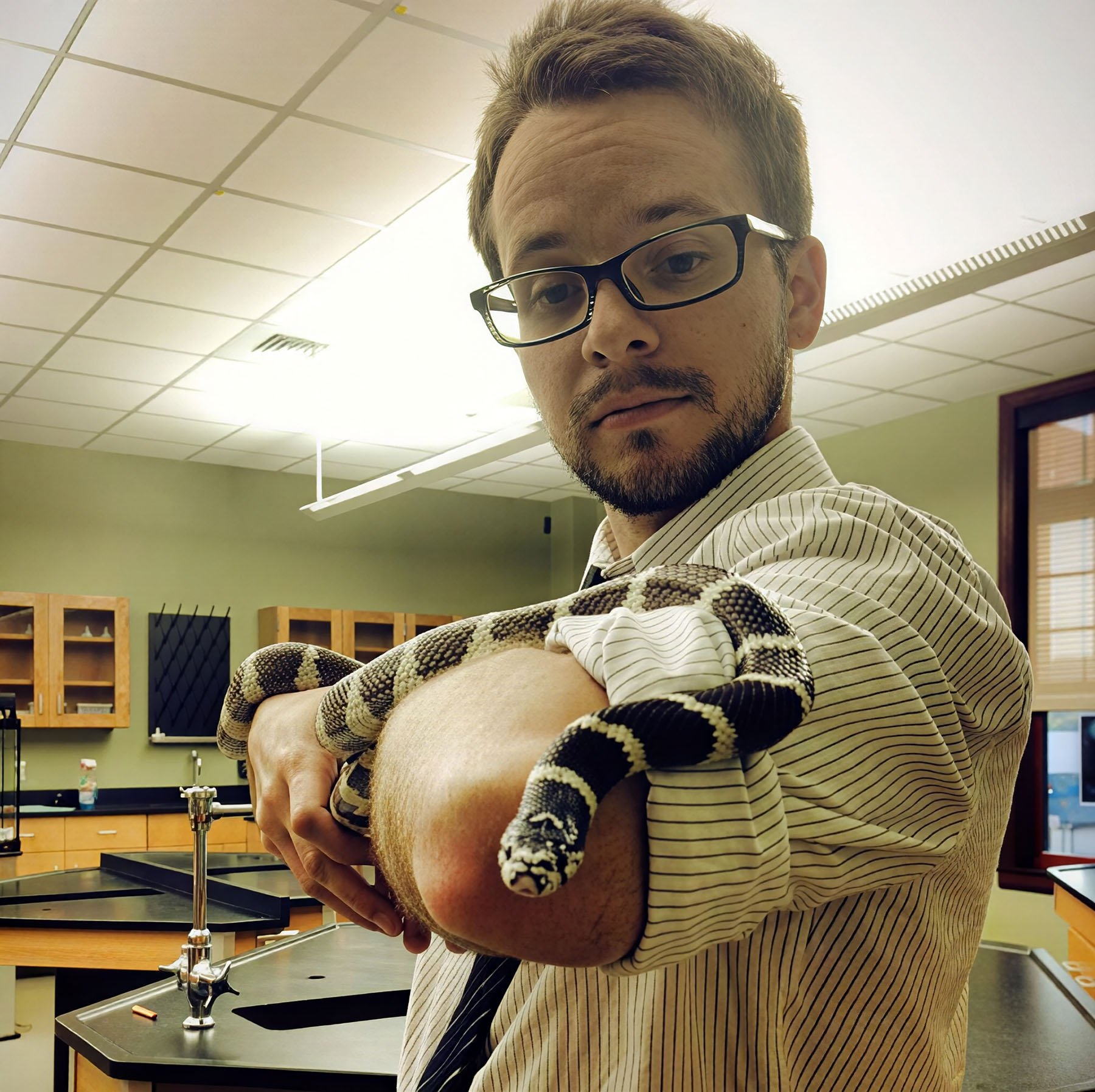Science teacher holding a black-and-white banded snake in a classroom.