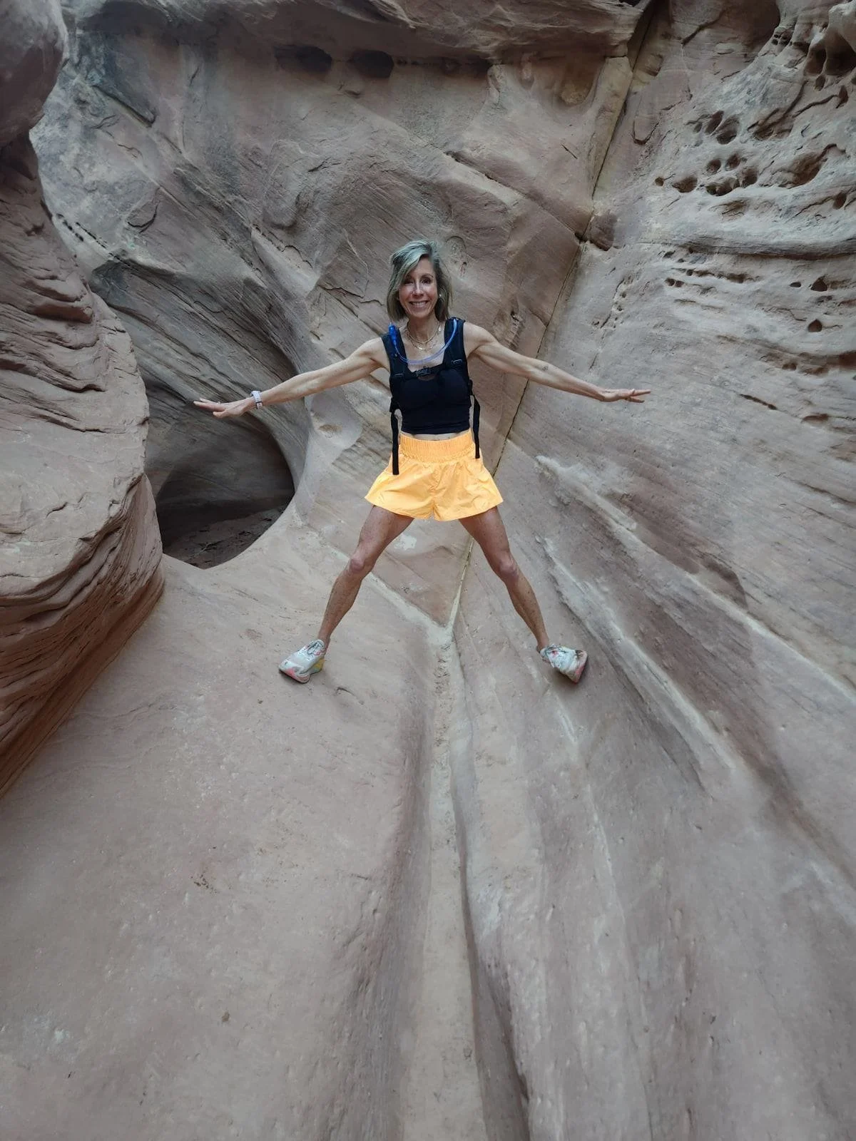 Katie Jensen poses with arms outstretched inside a narrow sandstone canyon, highlighting strength, balance, and exploration during a hiking adventure.