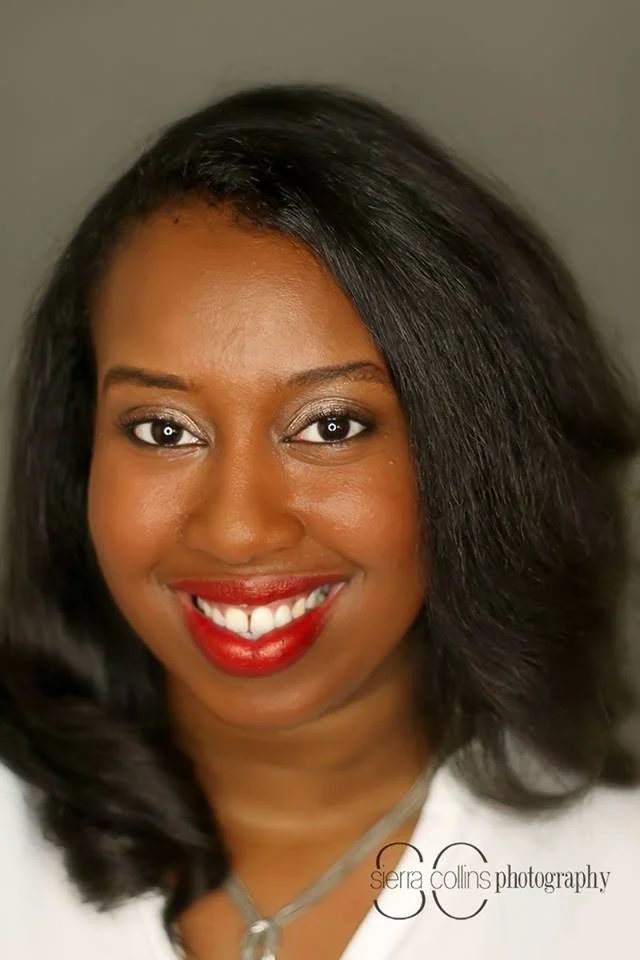 Smiling woman with shoulder-length dark hair wearing a white top against a neutral background.