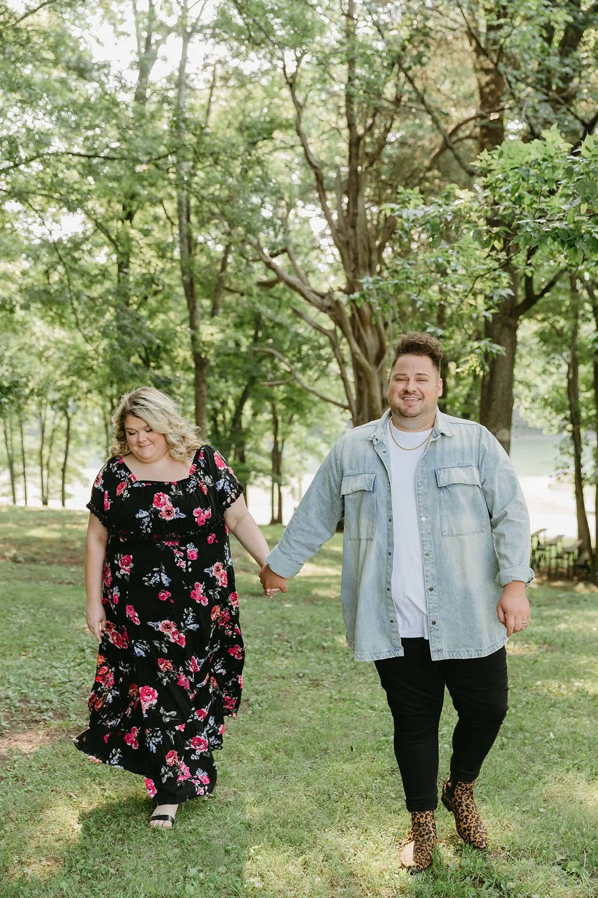 Woman and man walk through trees holding hands.
