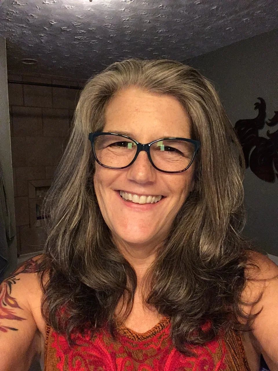 Smiling woman with long gray-brown hair and glasses.