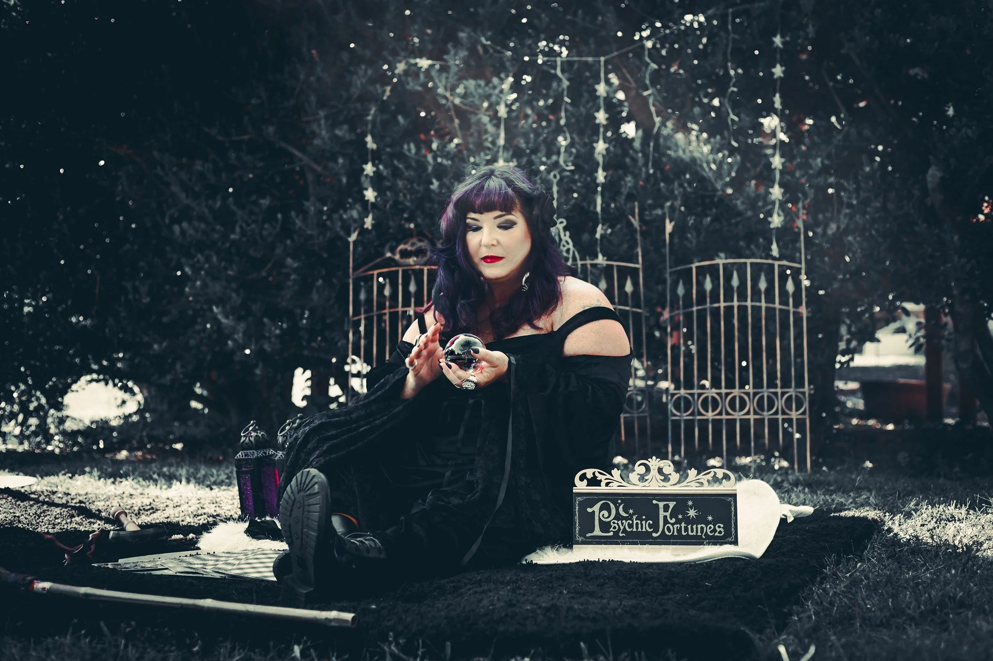 Psychic medium holding a crystal ball during an outdoor spiritual reading surrounded by mystical decor and twinkling lights.