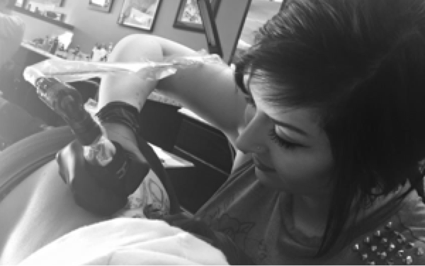 Black and white close-up of a tattoo artist tattooing a client in a tattoo shop.