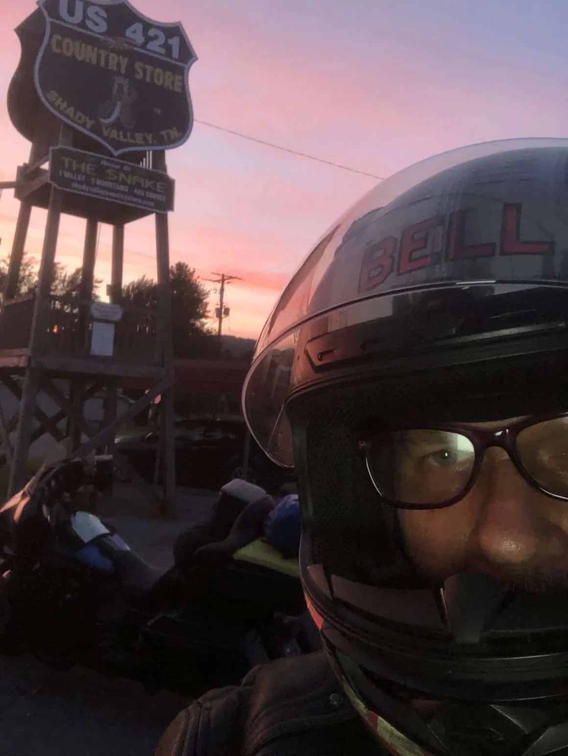 Motorcycle rider in helmet takes a selfie during dusk.