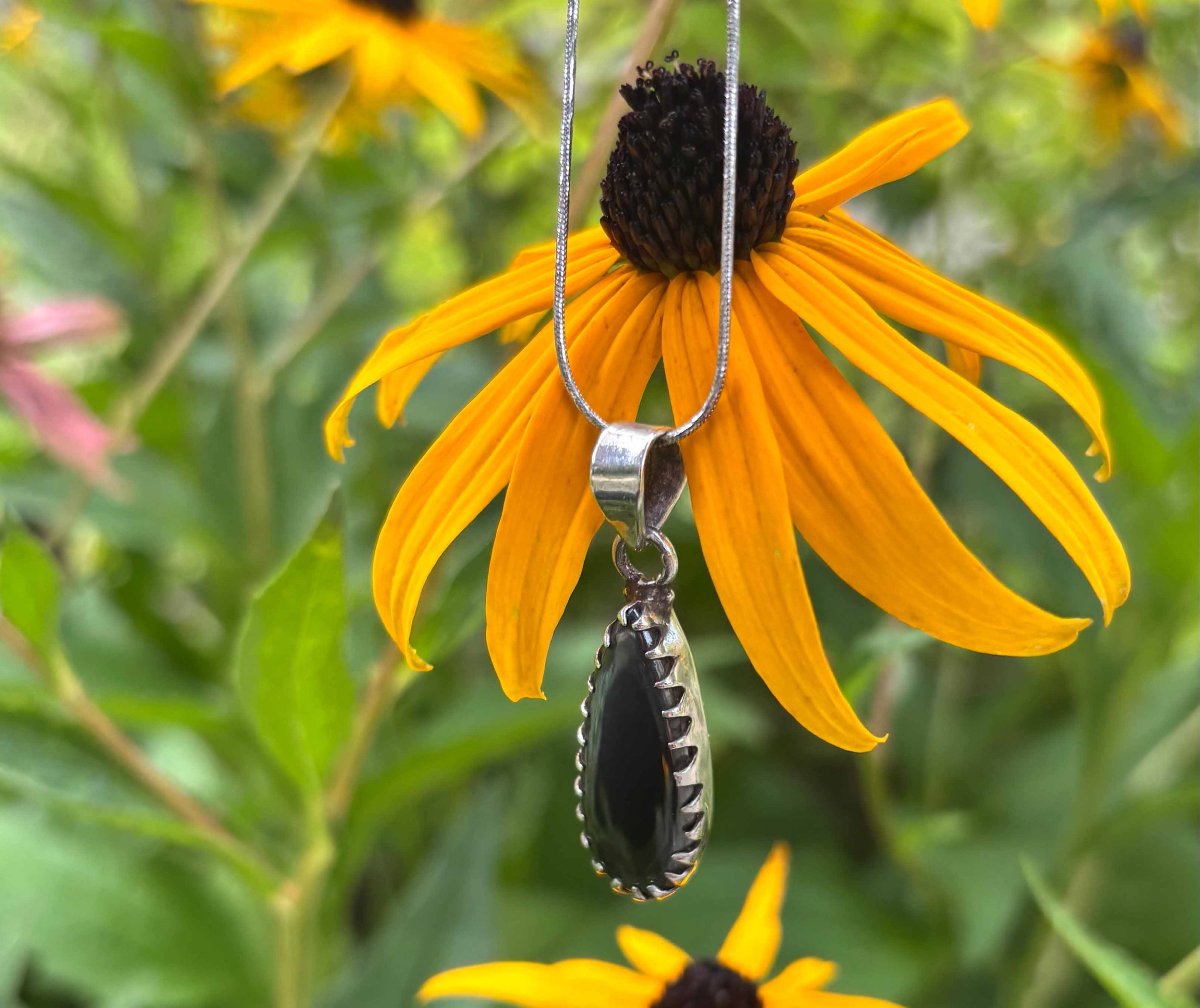 Polished black hematite pendant in a silver setting hanging in front of a bright yellow black-eyed Susan flower.