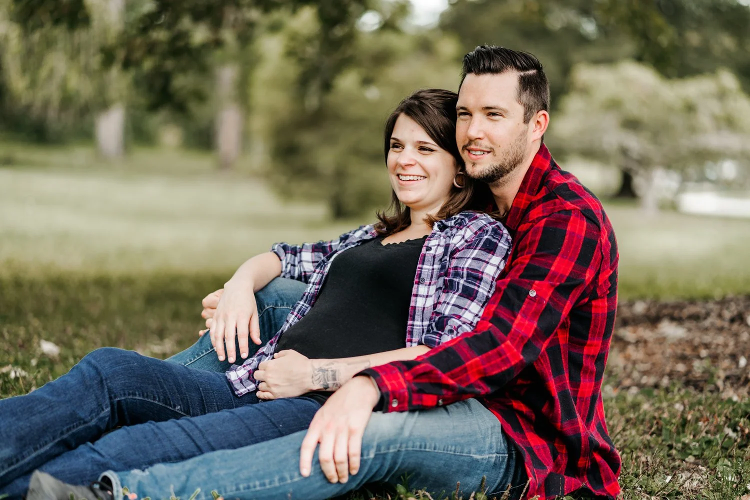 Couple sitting together outdoors during a maternity photo session in a grassy park.