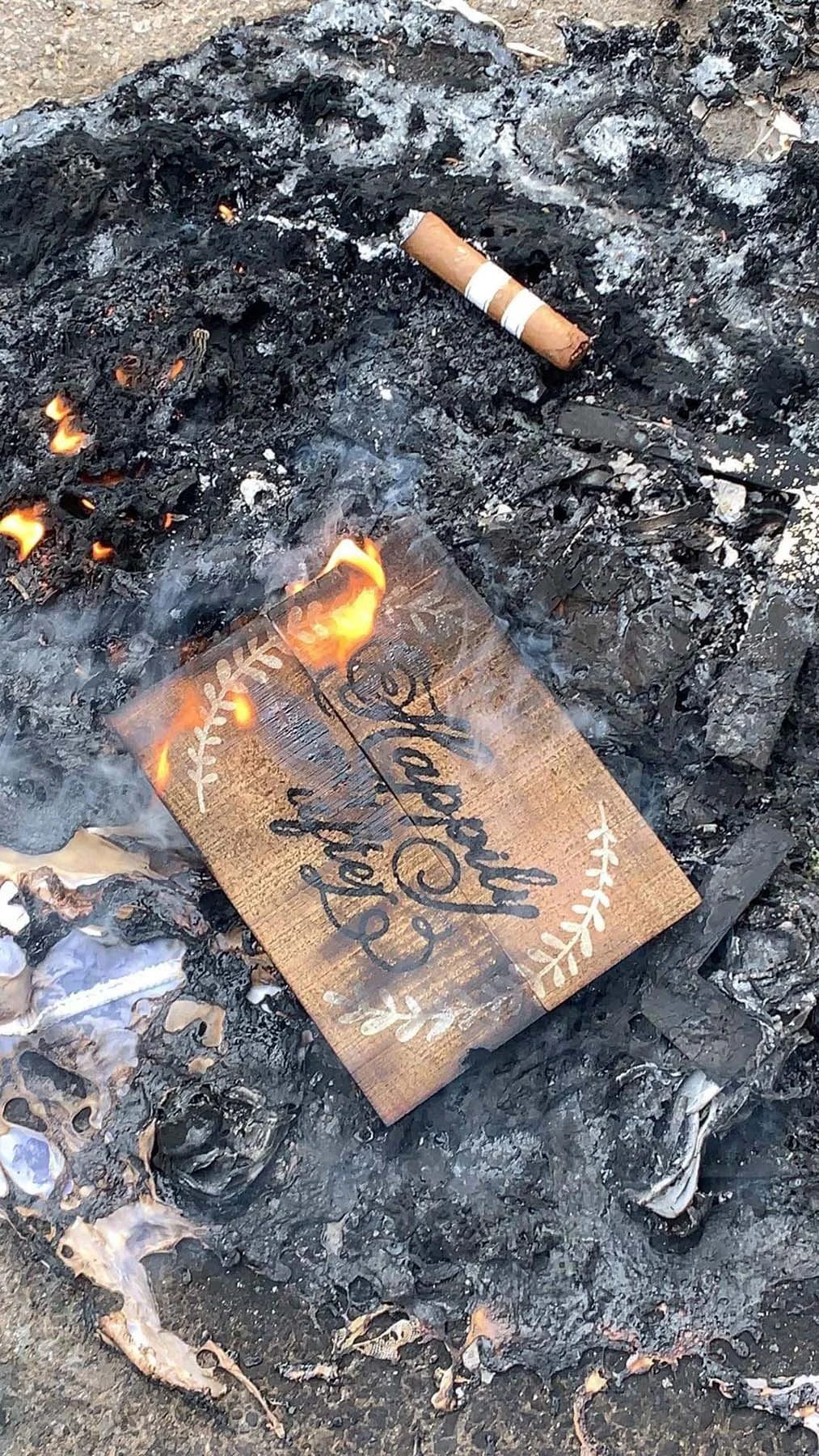 Burned wooden sign reading "Happily Ever after" in the ashes of a symbolic divorce fire ceremony.