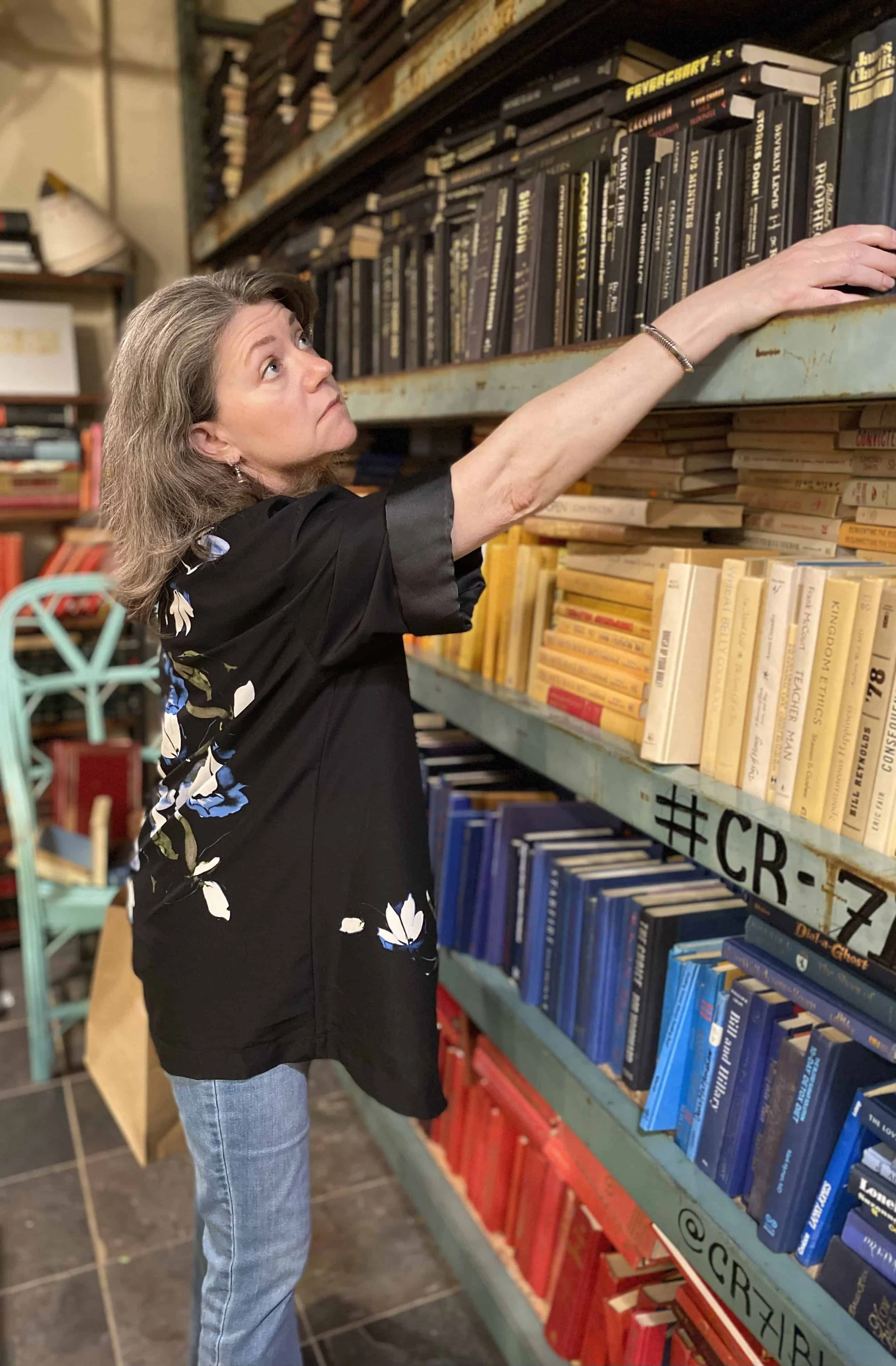 Silver-haired woman reaching up to organize books on a tall bookshelf.